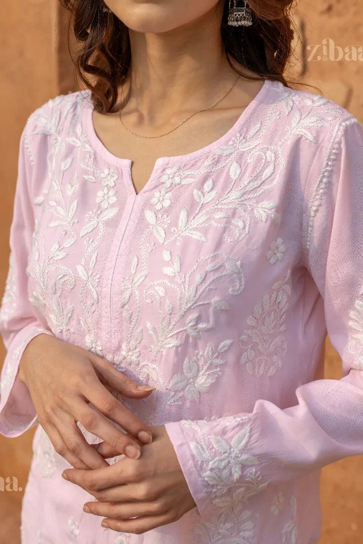 Model wearing a Pink Chikankari Kurti with intricate white embroidery, posing elegantly against a rustic wall in a traditional setting