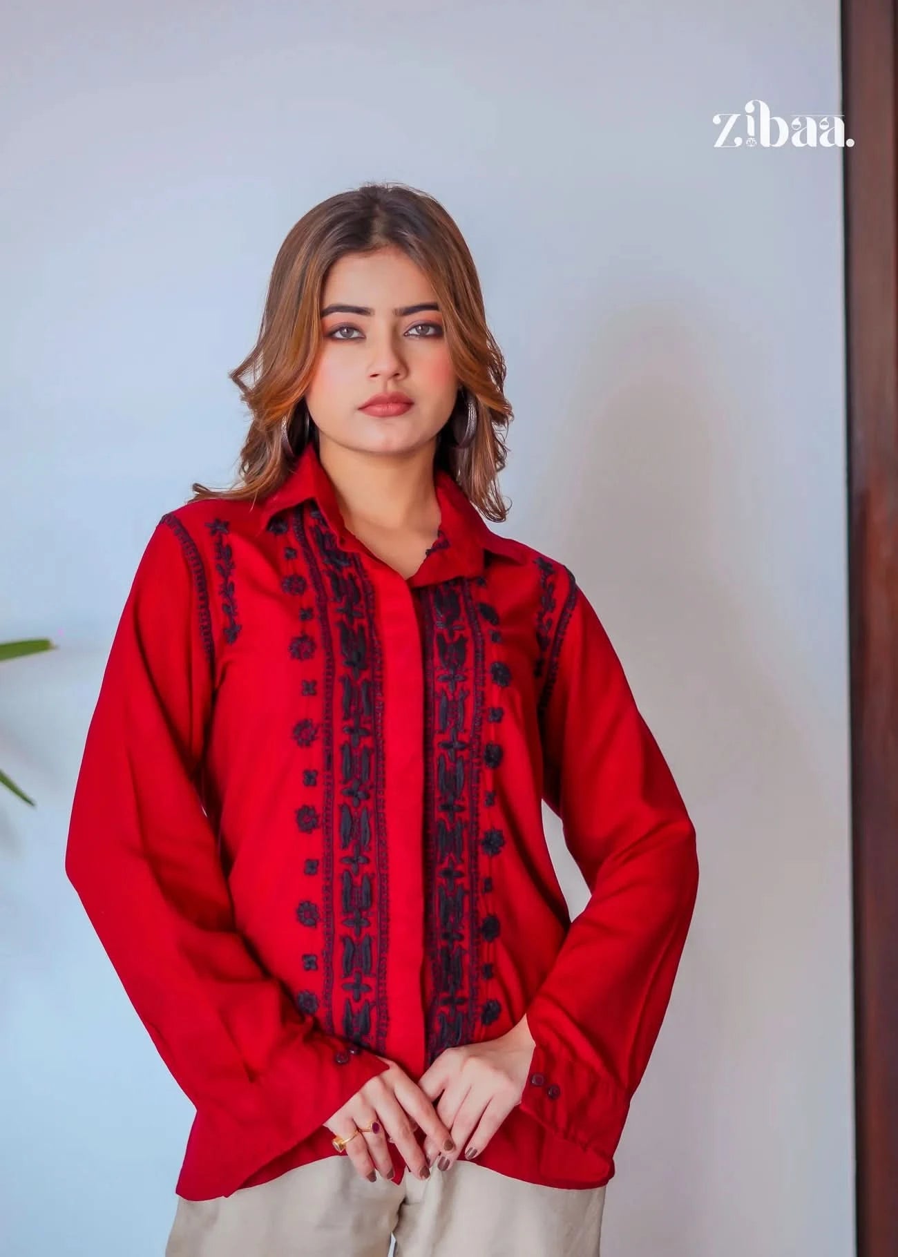 The model poses outdoors against a white wall, wearing a red chikankari shirt with intricate black embroidery.