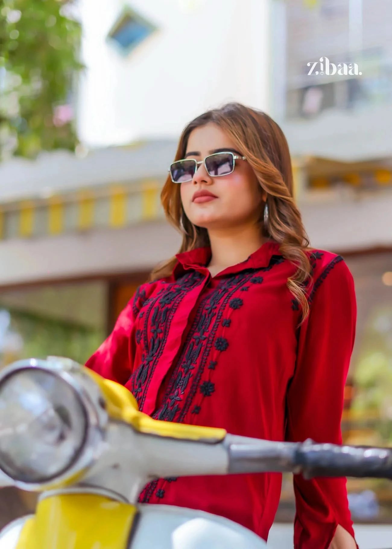 The model poses outdoors wearing sunglasses and a red chikankari shirt, with the black embroidery creating a striking contrast.