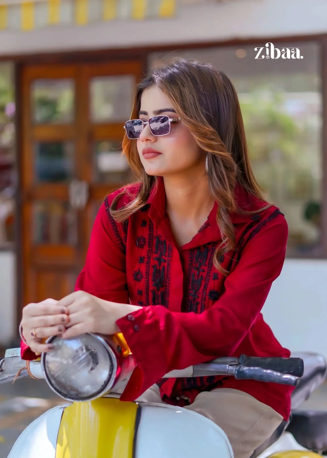 Resting her arms on the scooter, the model highlights the delicate black stitching on her red chikankari shirt while posing outdoors.