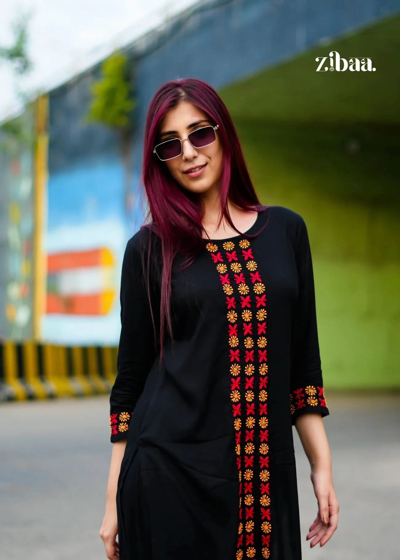 Woman wearing a black chikankari kurta set with colorful embroidery, standing outdoors.