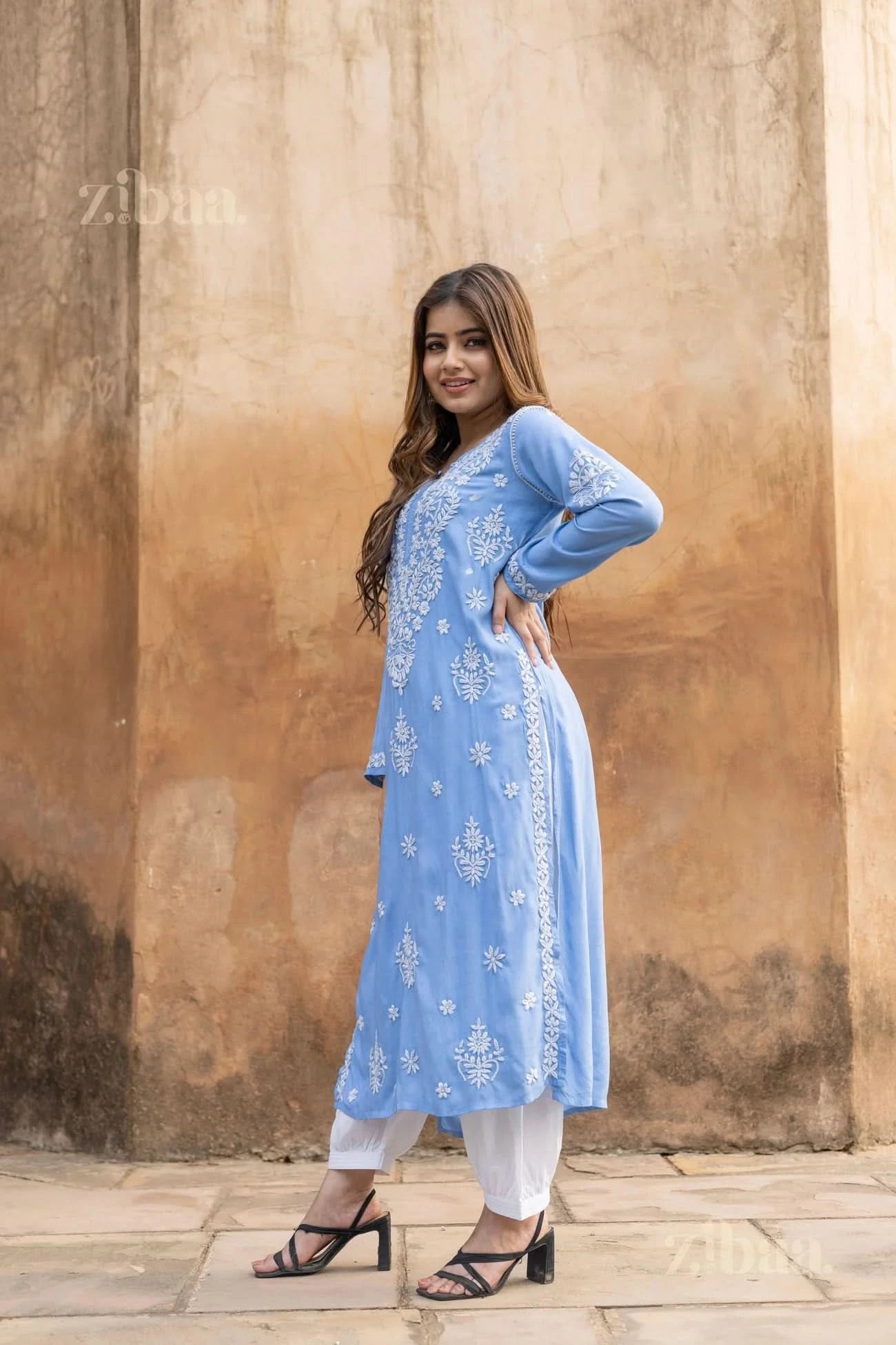 Model in Blue Chikankari Kurta with white embroidery styled with white pants shows grace against a rustic backdrop.