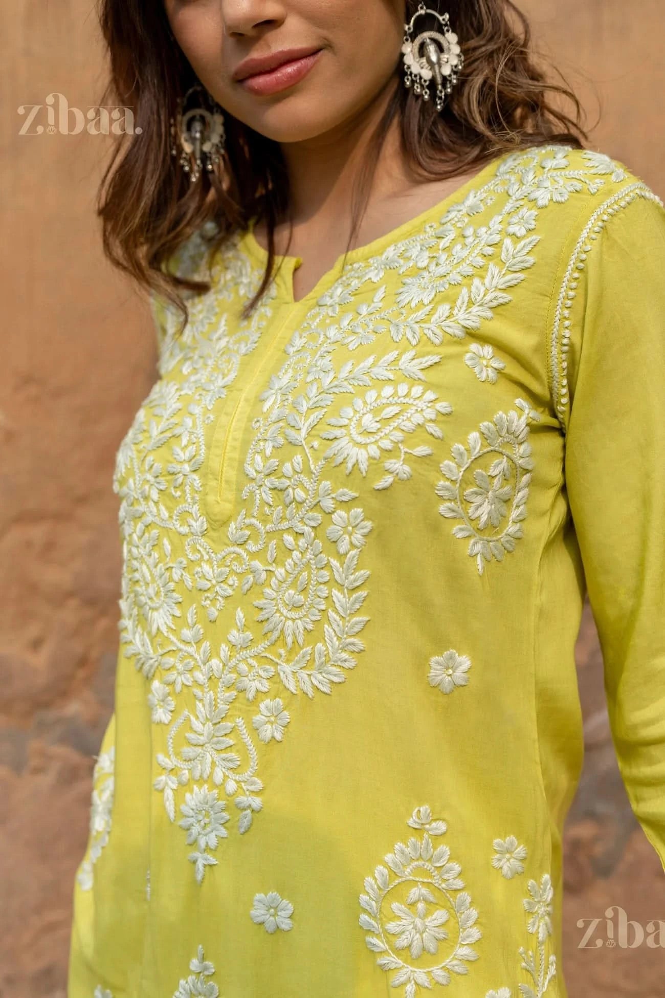 A woman stands with a soft smile, tilting her head, wearing a lime green Chikankari long kurti, showcasing detailed white embroidery.