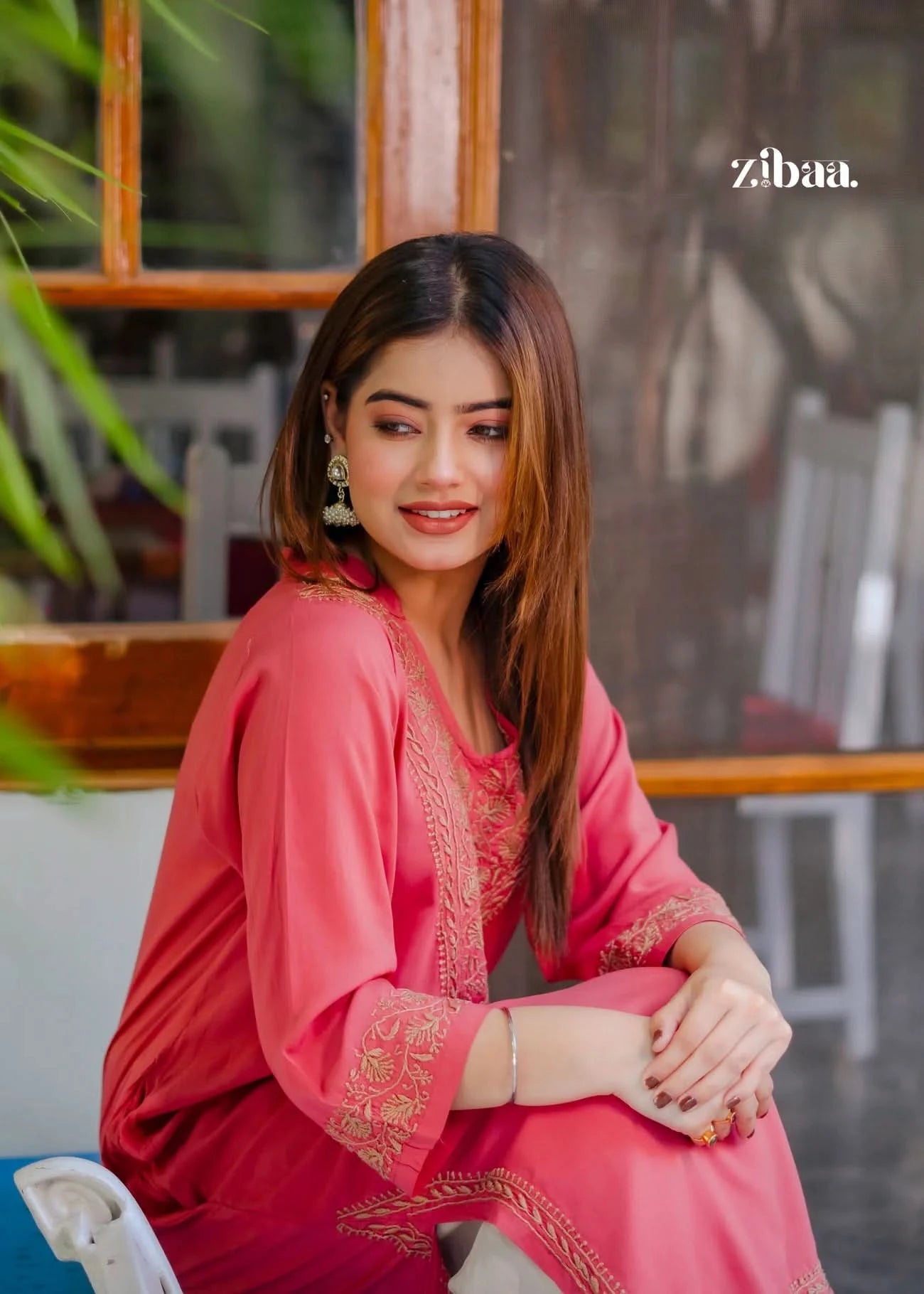 Sitting comfortably, the model highlights the elegant chikankari work on her coral kurti with a relaxed pose.