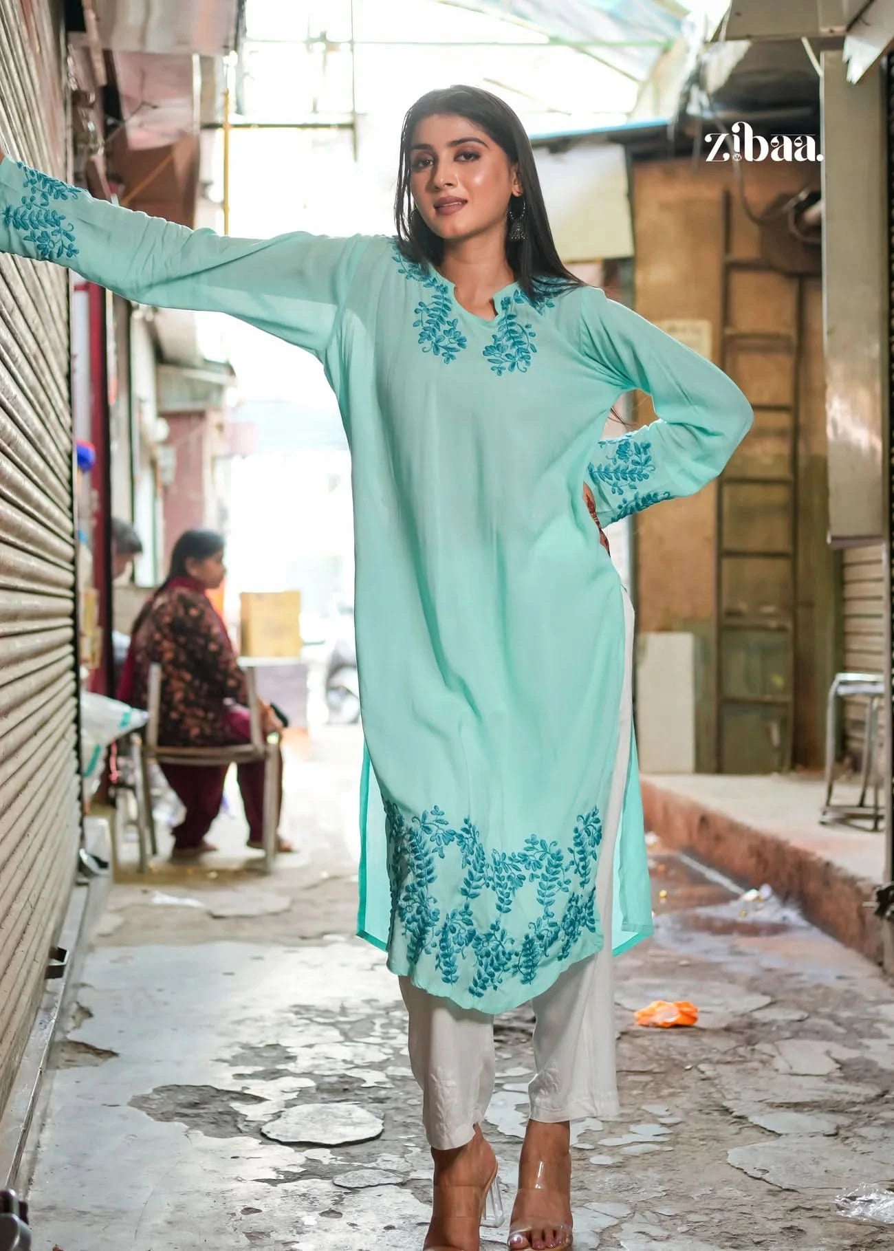 A woman looks graceful in a light blue chikankari kurti, standing on a street. The intricate embroidery highlights a blend of modern style and traditional craftsmanship