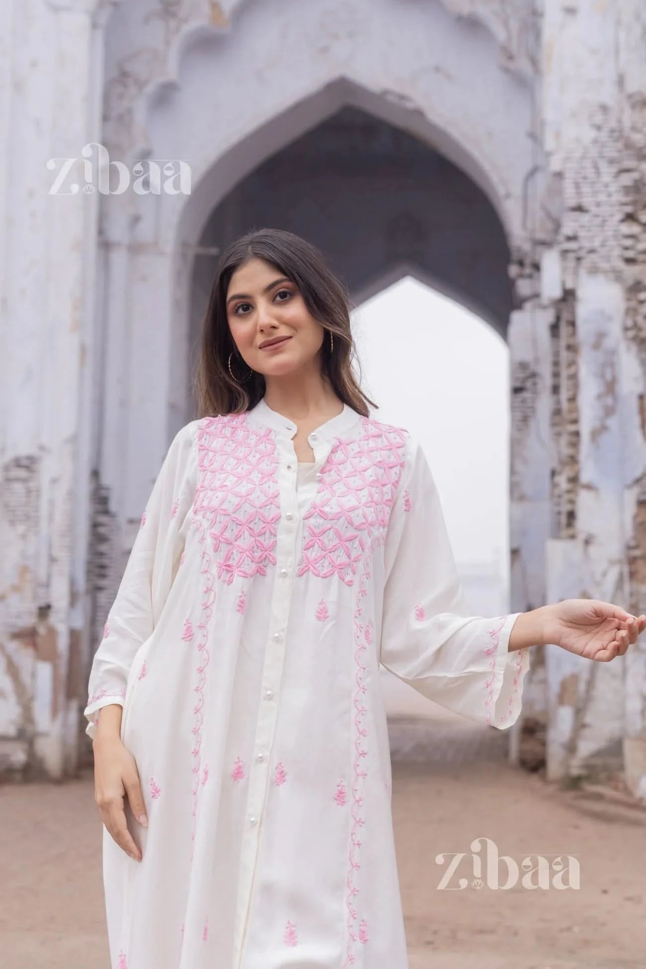 Woman wearing a white chikankari kurta with pink geometric embroidery, standing outdoors in natural light.