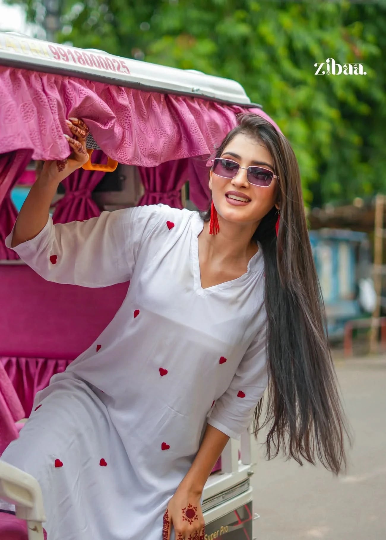 The model poses wearing a white chikankari kurti with heart motifs while sitting in an auto-rickshaw on a street.