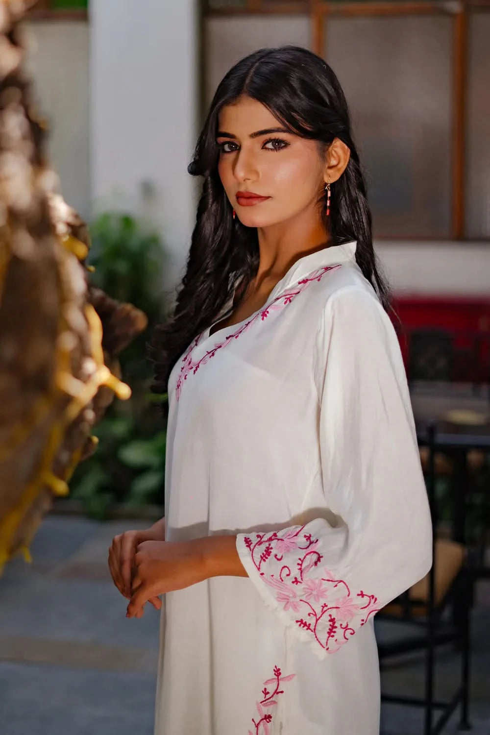 White chikankari kurti with pink embroidery patterns on woman, shown outdoors.
