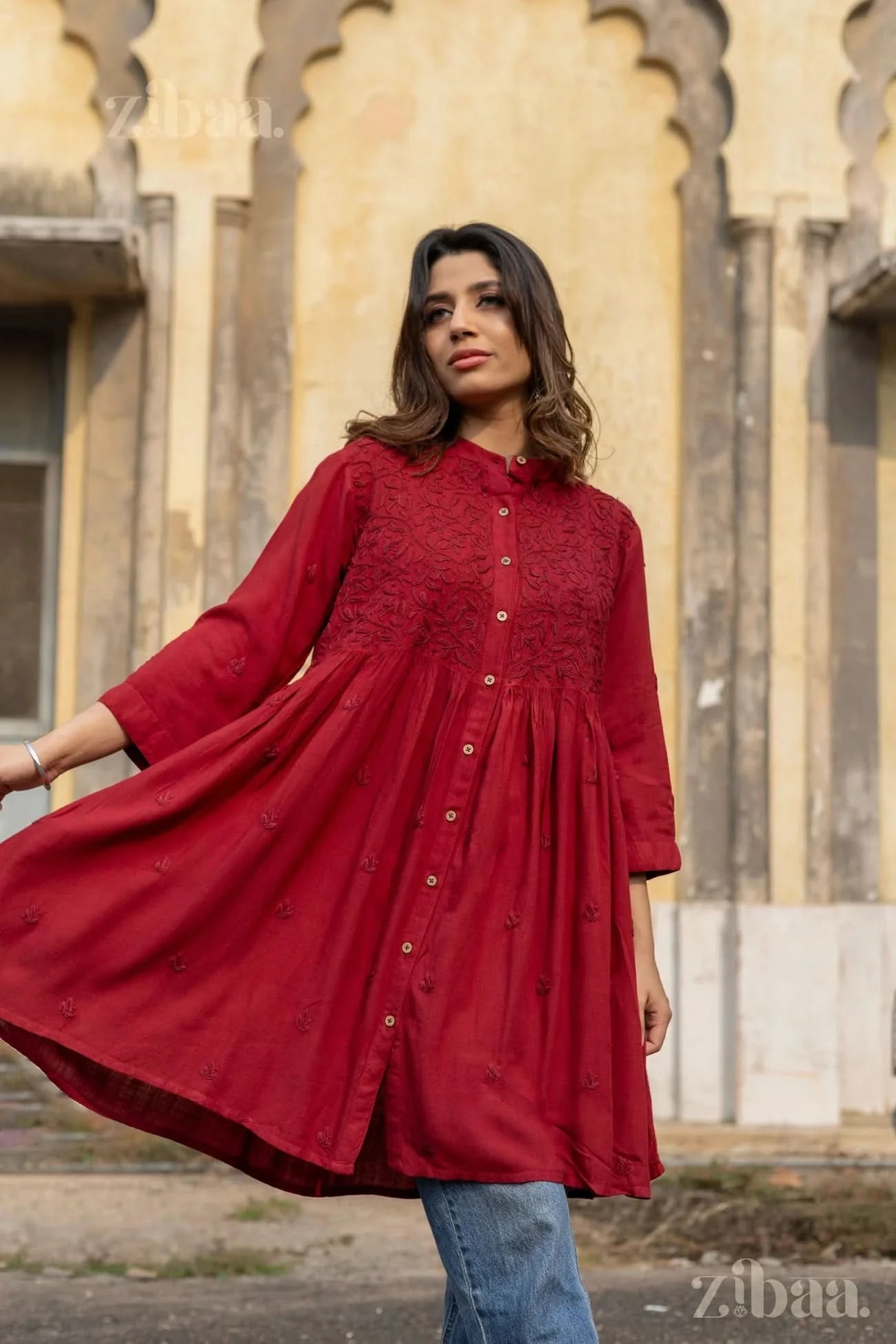 A woman twirls slightly, showing the flowy maroon Chikankari top with tonal embroidery and button-down detailing, paired with jeans.