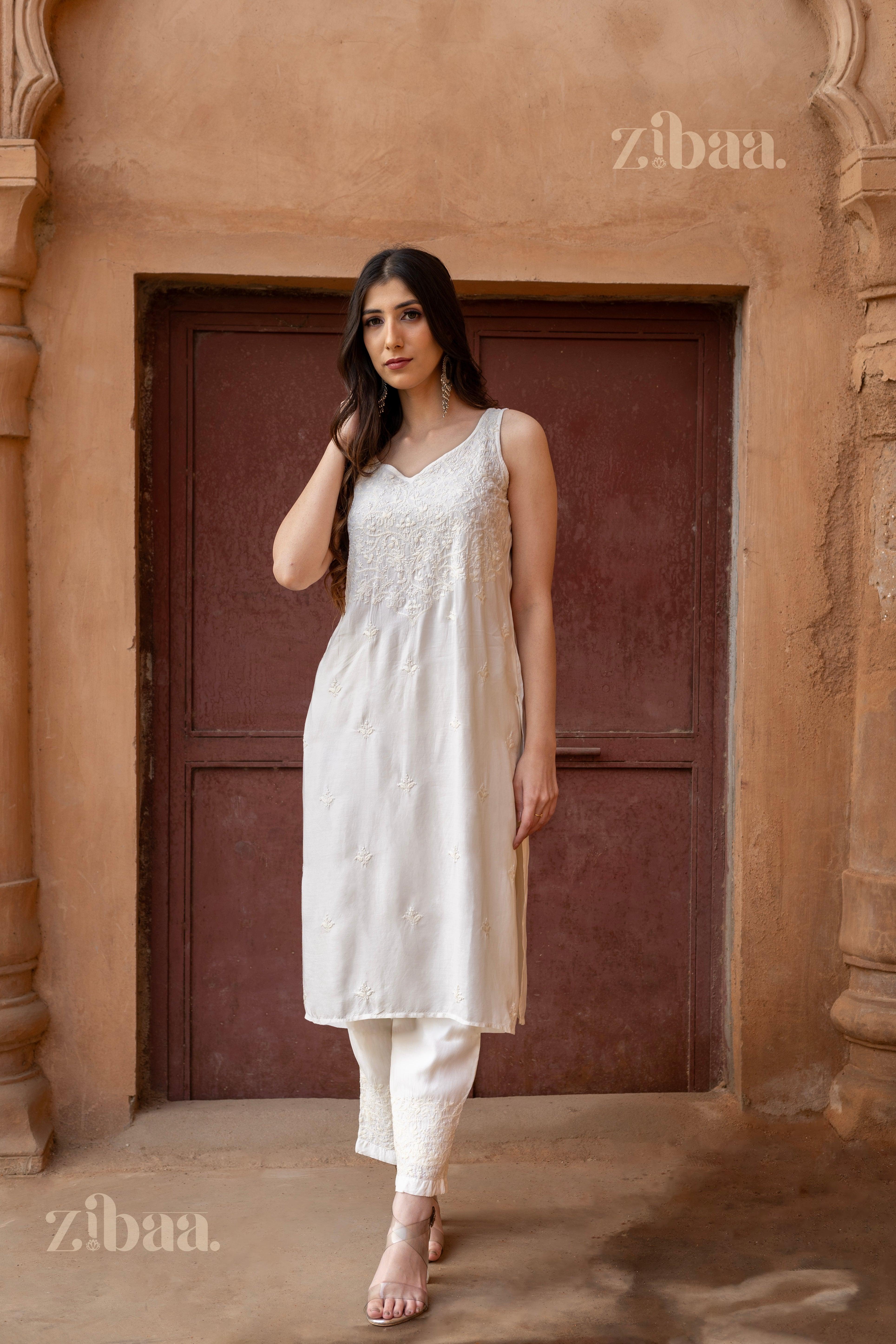 Model wearing a sleeveless Chikankari Kurta Set in white, featuring delicate embroidery, posing in a rustic architectural setting.