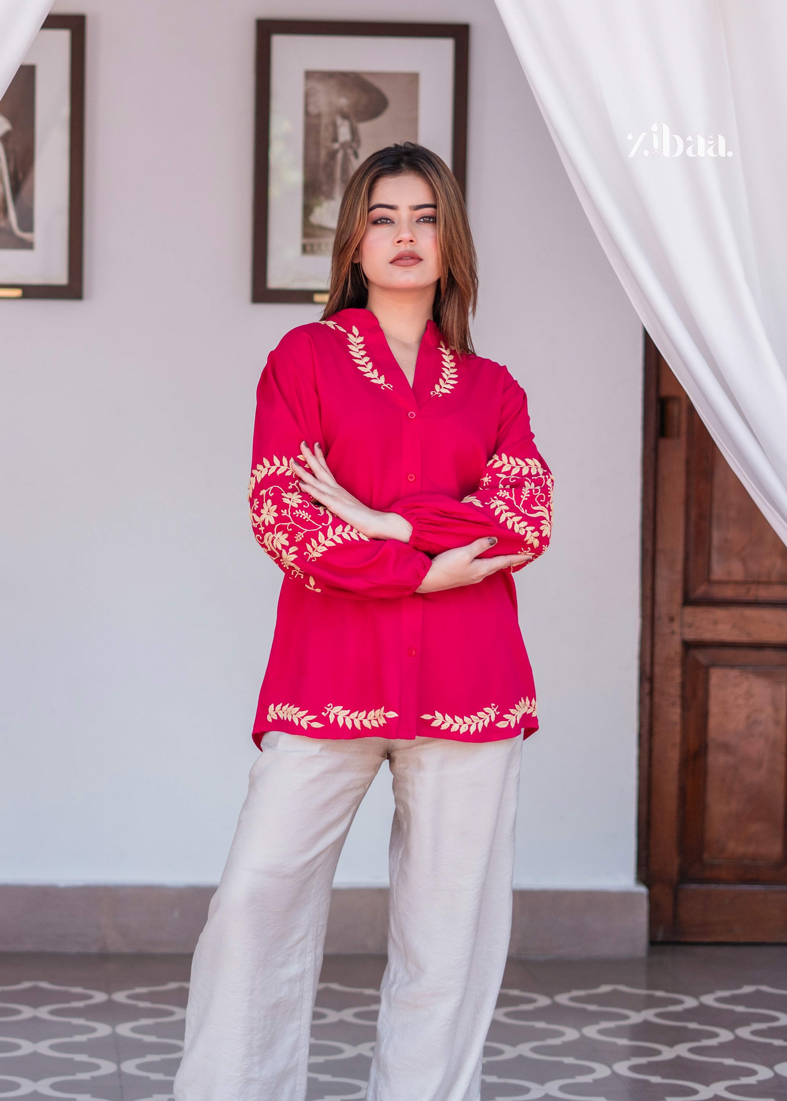 The model stands near a wooden door in a Traditional Pink Embroidered Kurta Outfit. Traditional Pink Embroidered Kurta Outfit showcases golden detailing across sleeves and hem. Beige trousers add balance to the bold kurta.