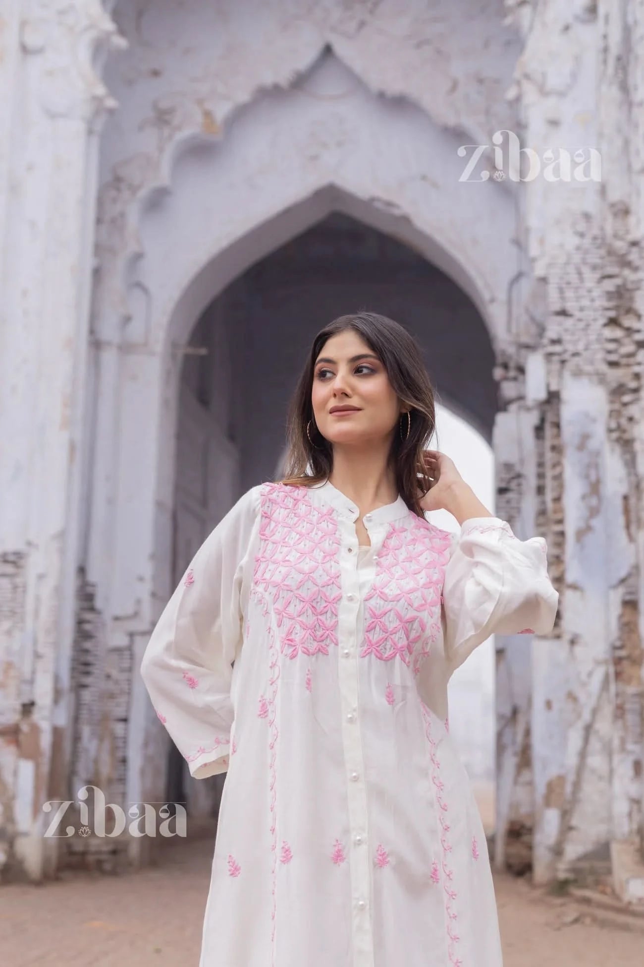 Contemporary style featuring a white chikankari kurta with hand-embroidered pink geometric designs, captured outside.