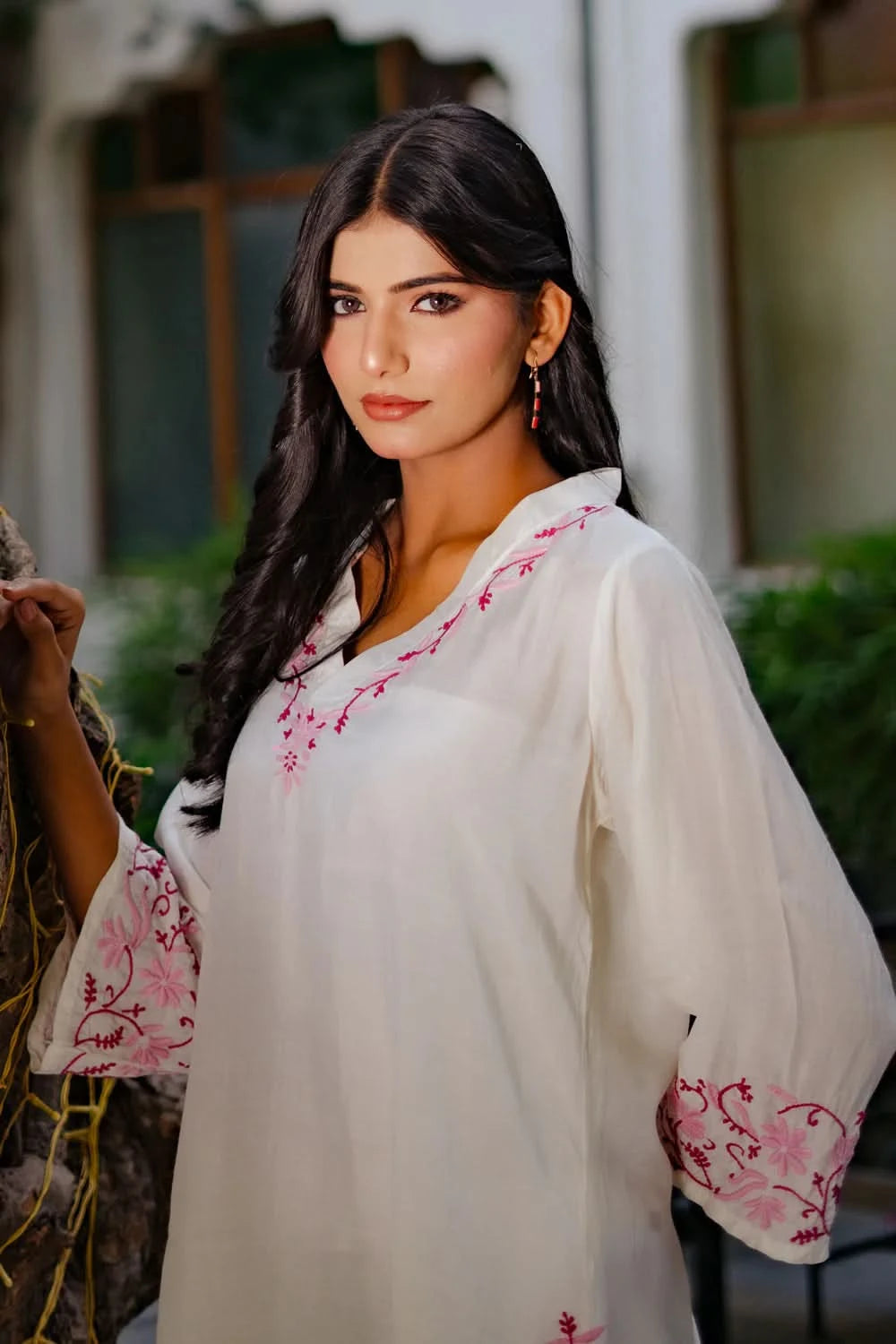 Woman wearing a white chikankari kurti with pink embroidery in an outdoor setting.