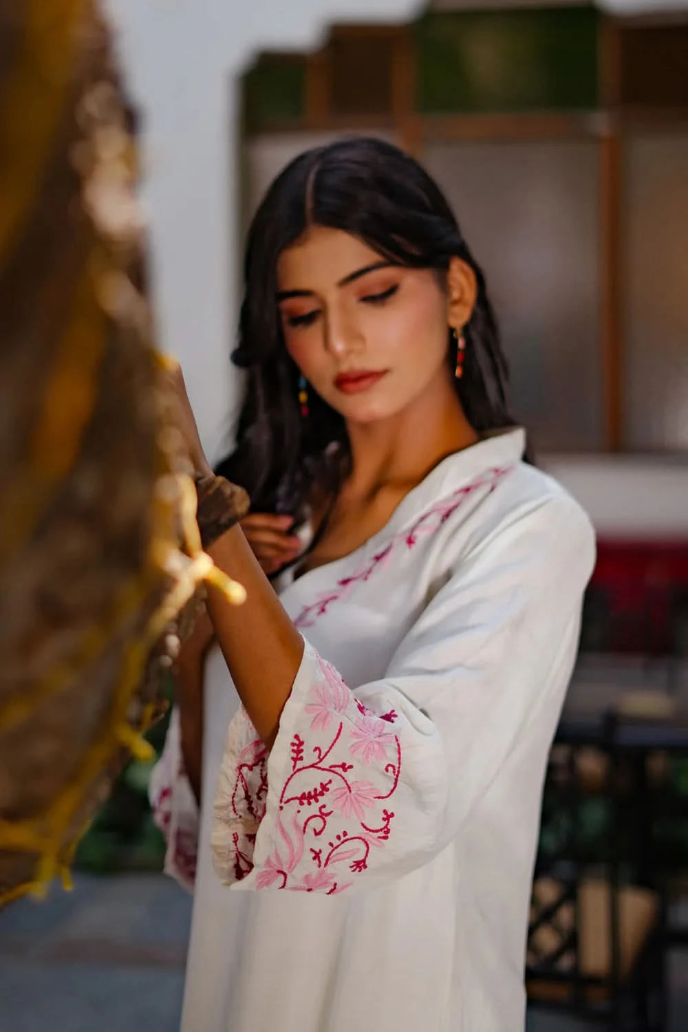 Side view of woman wearing white chikankari kurti with pink embroidery outdoors.