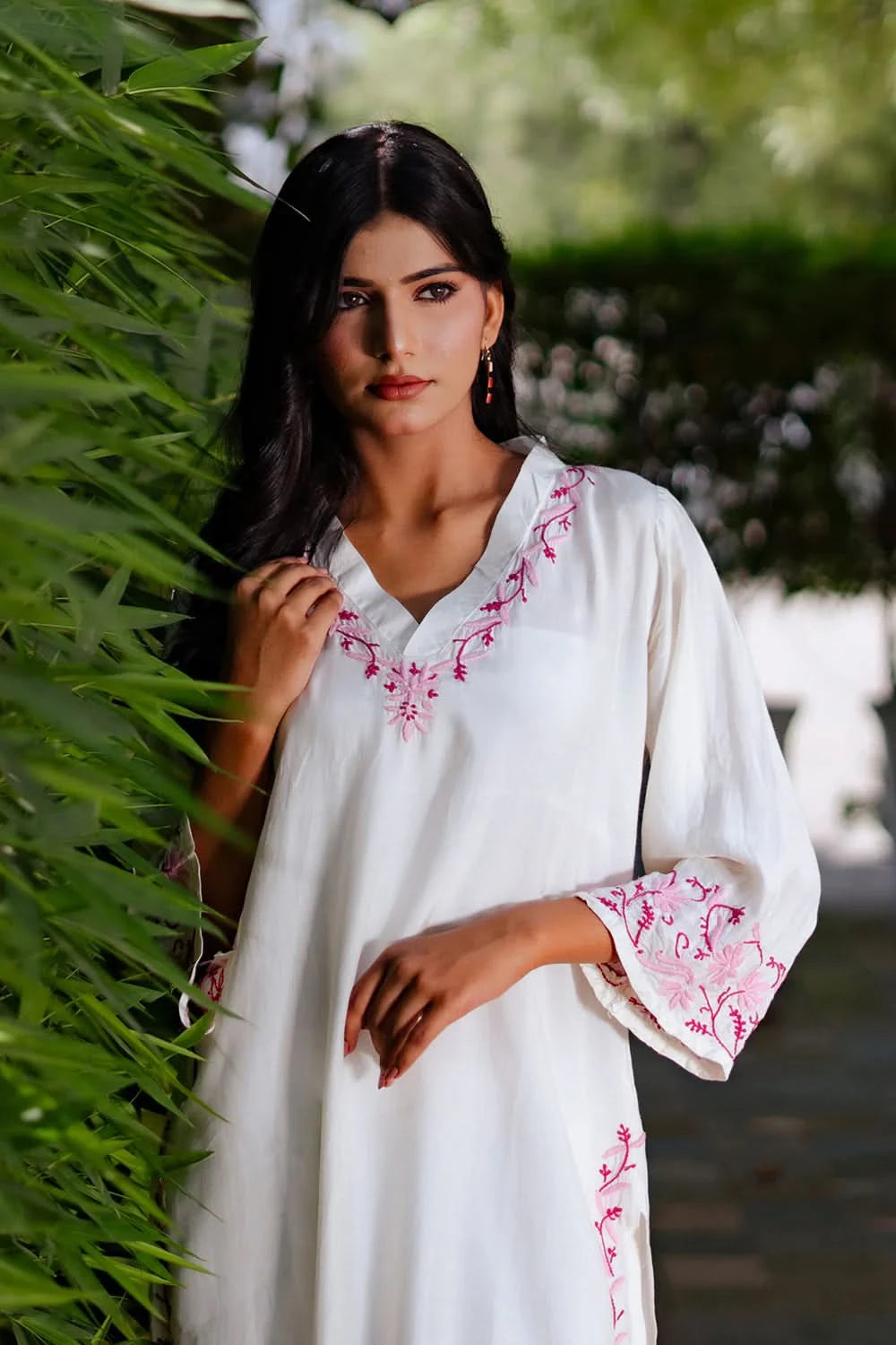Woman wearing a white dress with pink embroidery standing outdoors.