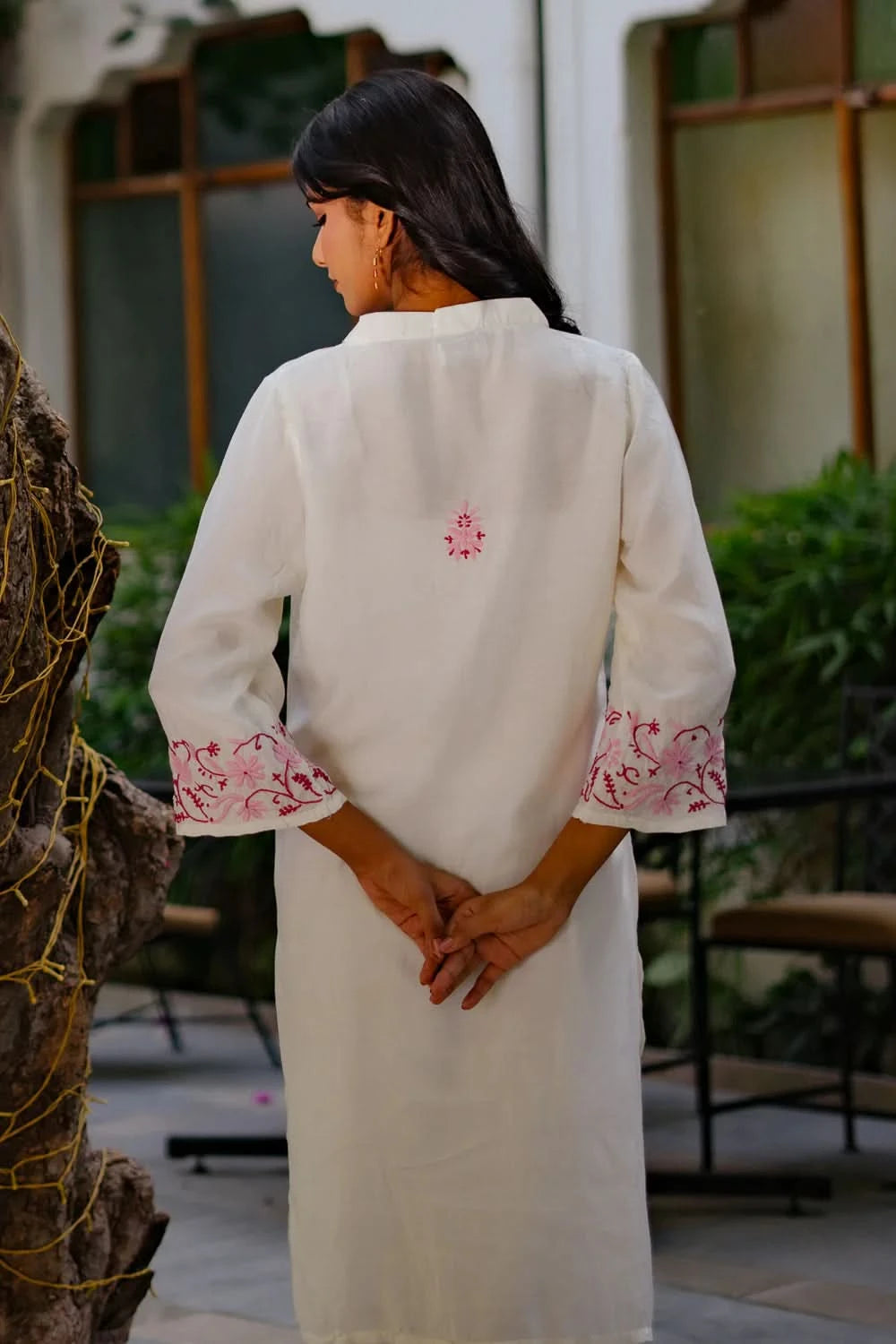 Back shot of a woman wearing a white chikankari kurti with pink embroidery in an outdoor setting.