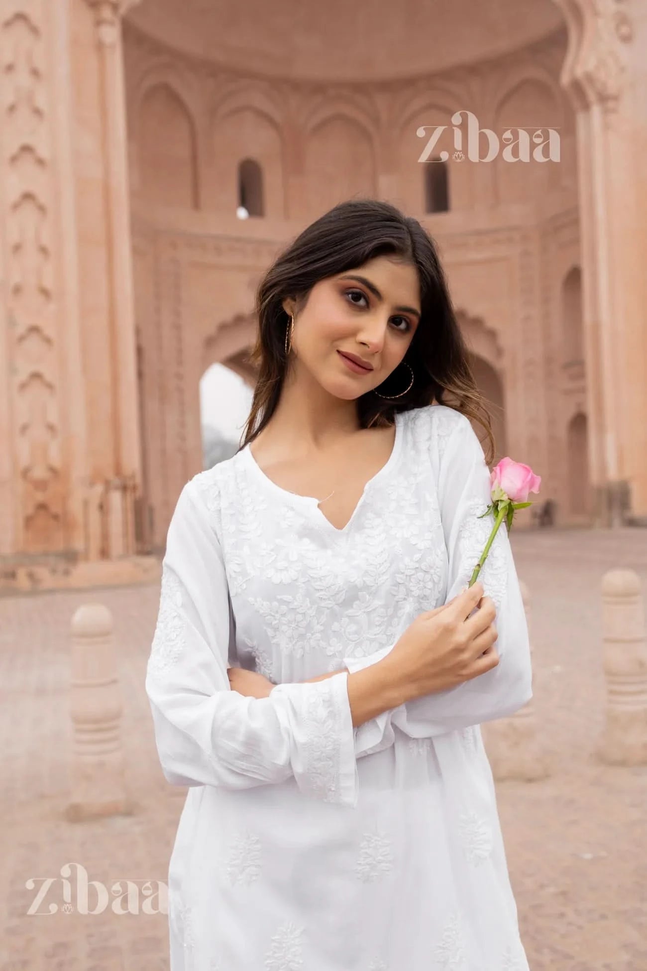 Woman wearing a white short chikankari kurti standing outside an architectural backdrop.