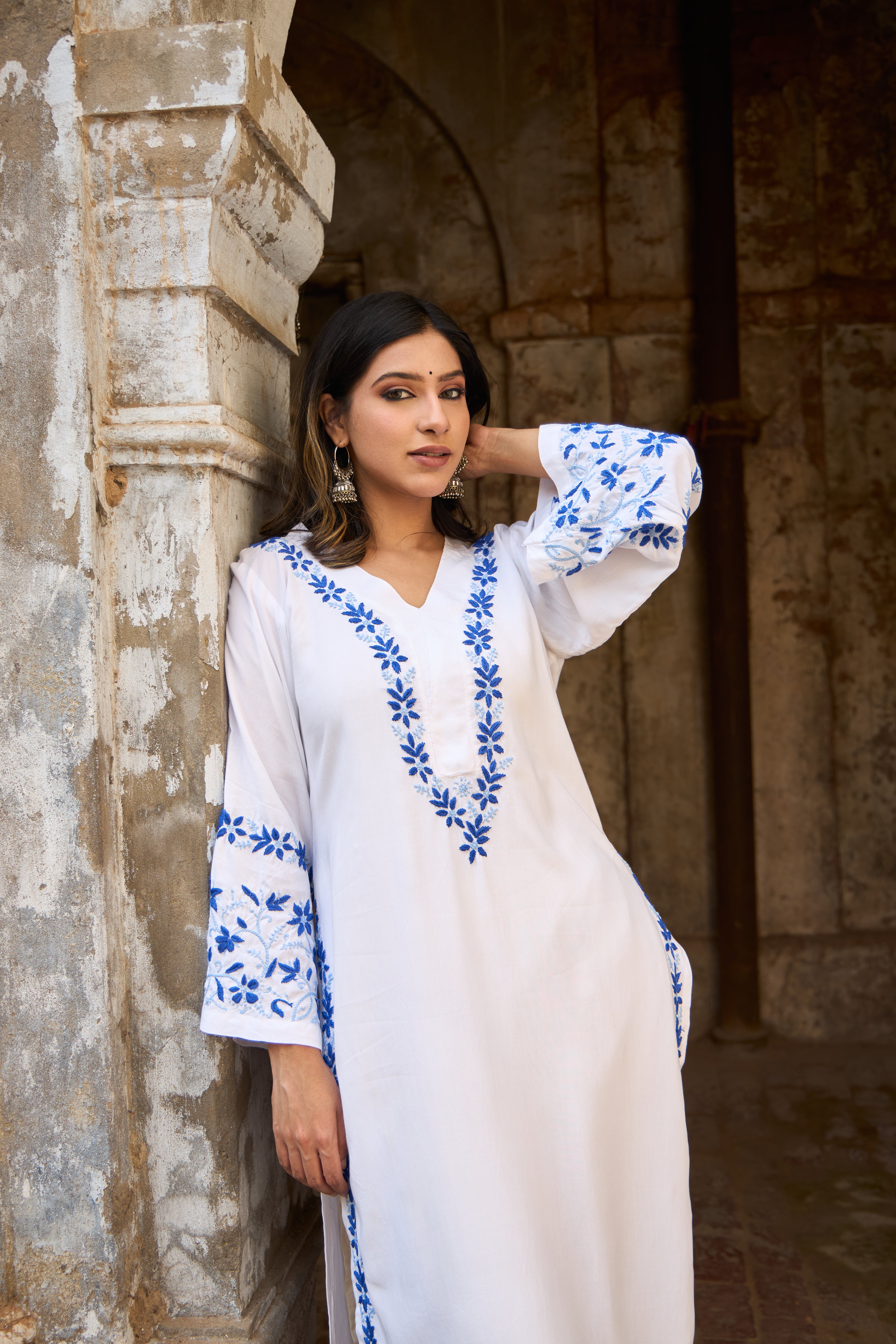 Woman wearing a White Chikankari Kurta with blue embroidery standing against a stone wall.