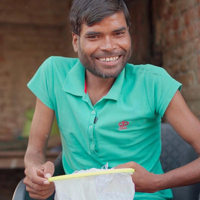 A Chikankari artisan is smiling in the image while stitching a kurta