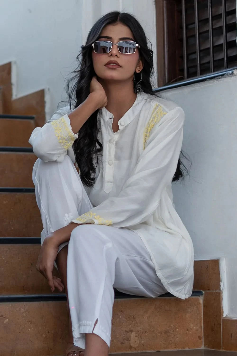 Woman in a white outfit with yellow accents sitting on steps.