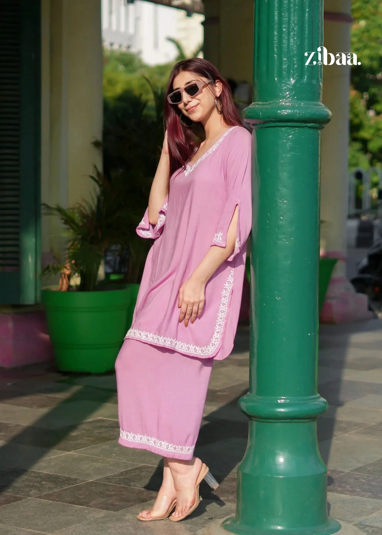 Woman in a pink outfit standing next to a green pole with 'zibaa' branding.