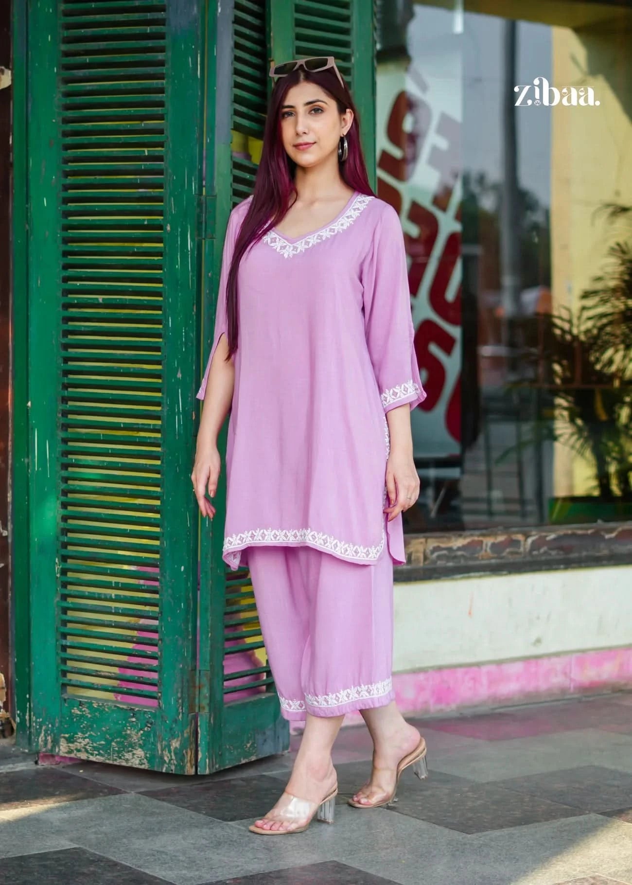 Woman in a pink outfit standing in front of a green door with 'zibaa' branding.