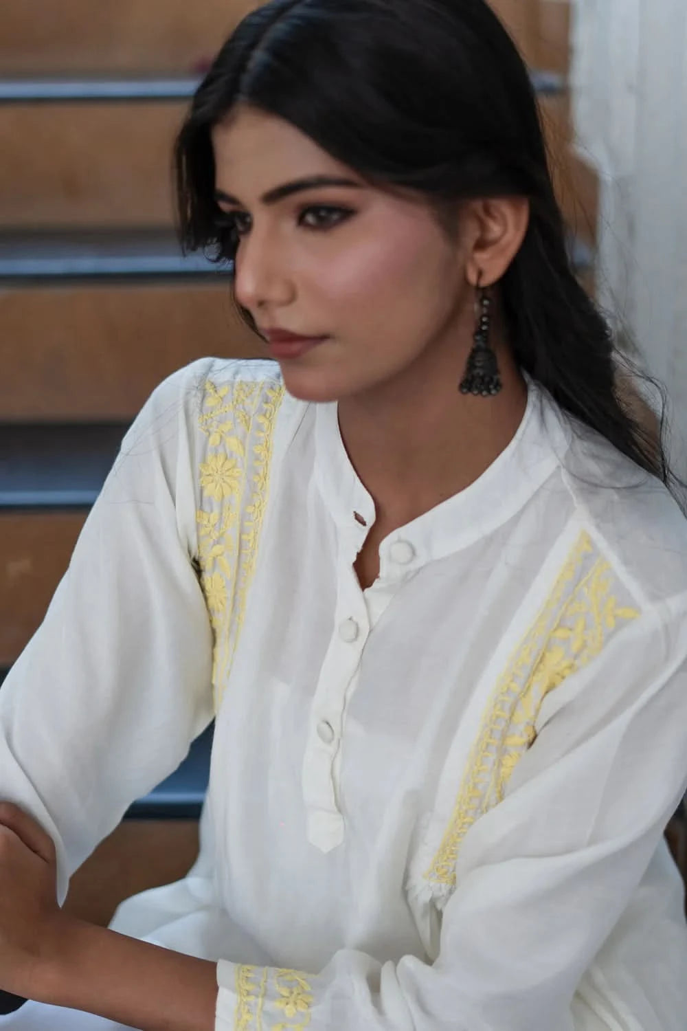 Woman wearing a white embroidered outfit with yellow details, sitting on steps.