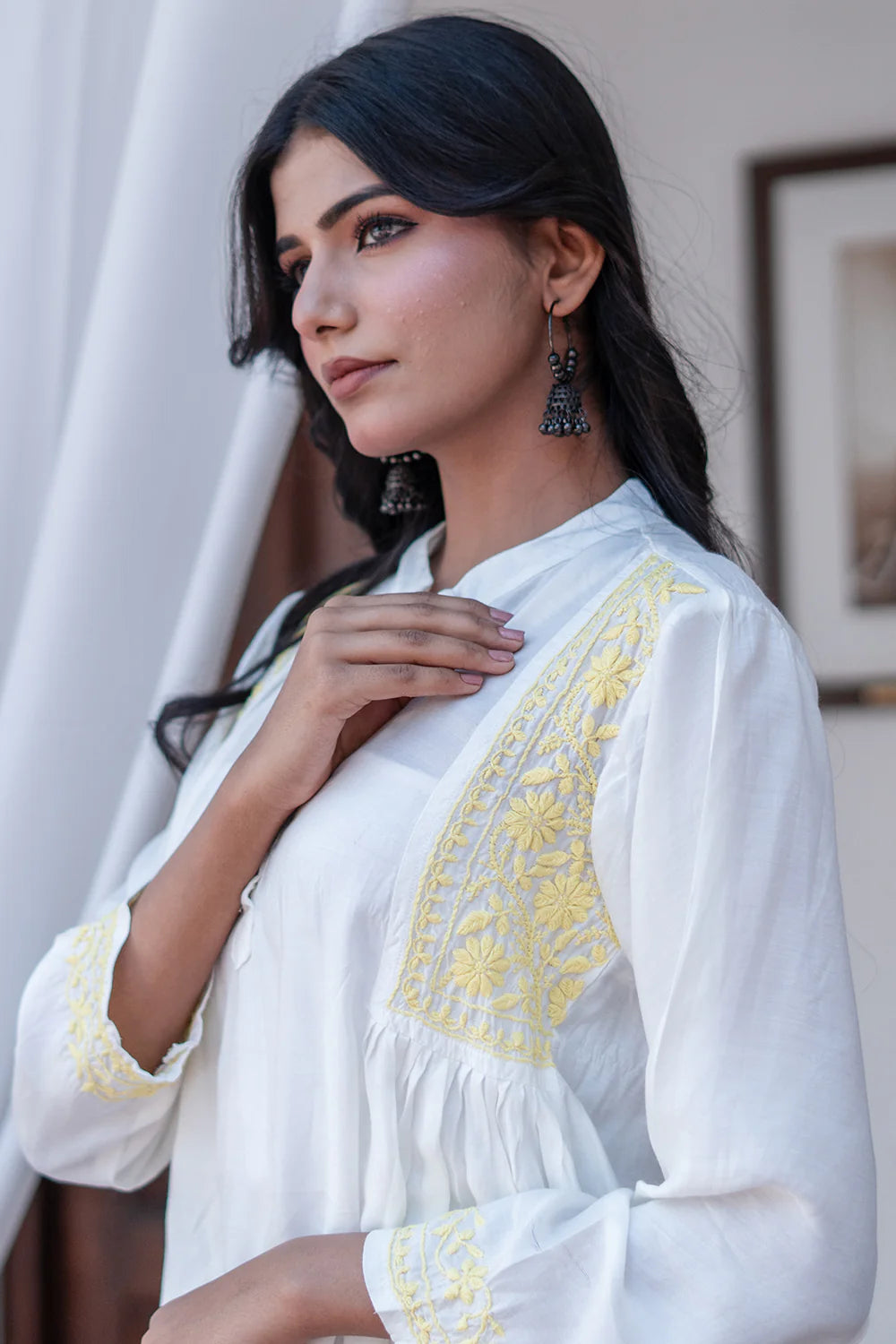 Woman wearing a white blouse with yellow embroidery indoors