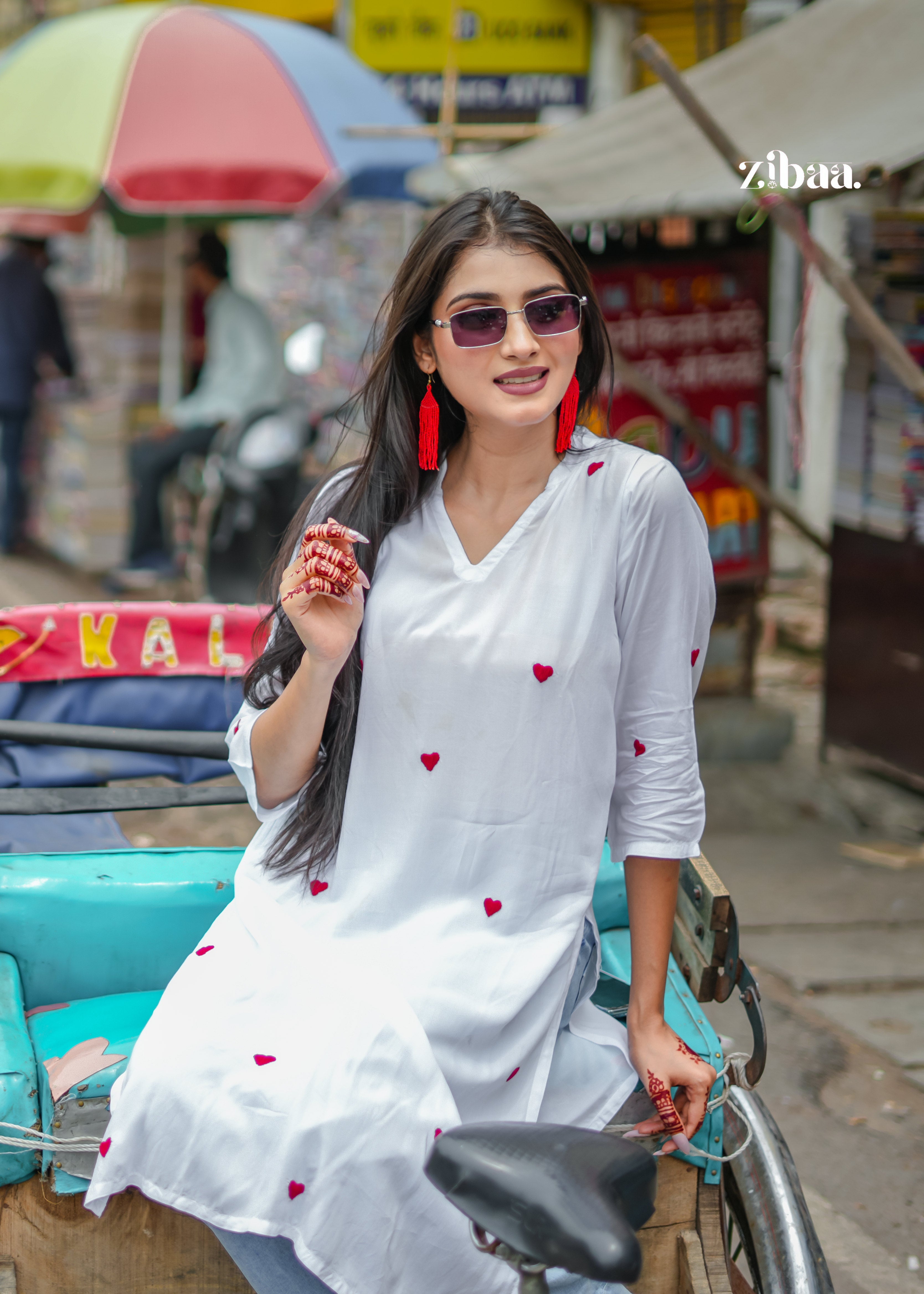 Woman in a white dress with red heart patterns sitting on a rickshaw in an urban setting.