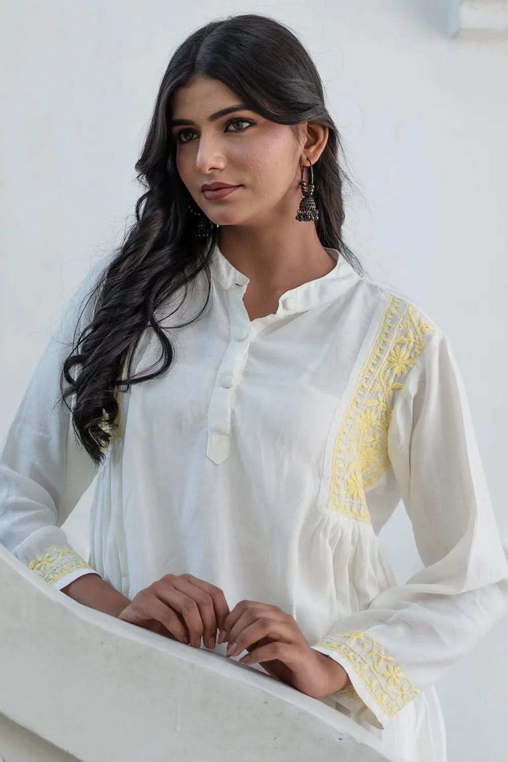 Woman wearing a white embroidered blouse with yellow details against a light background