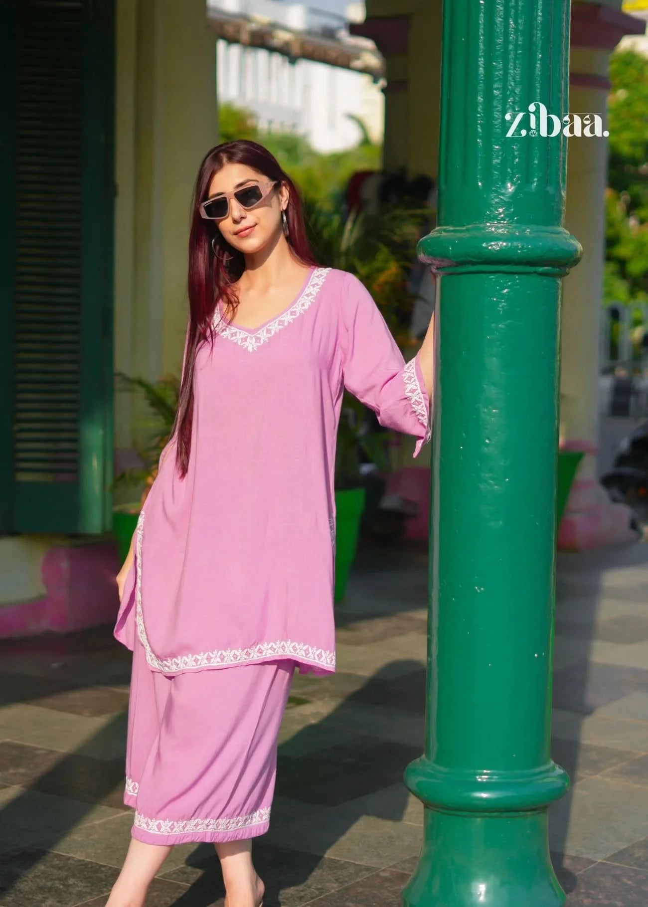 Woman in a pink outfit standing next to a green pole with 'zibaa' branding.
