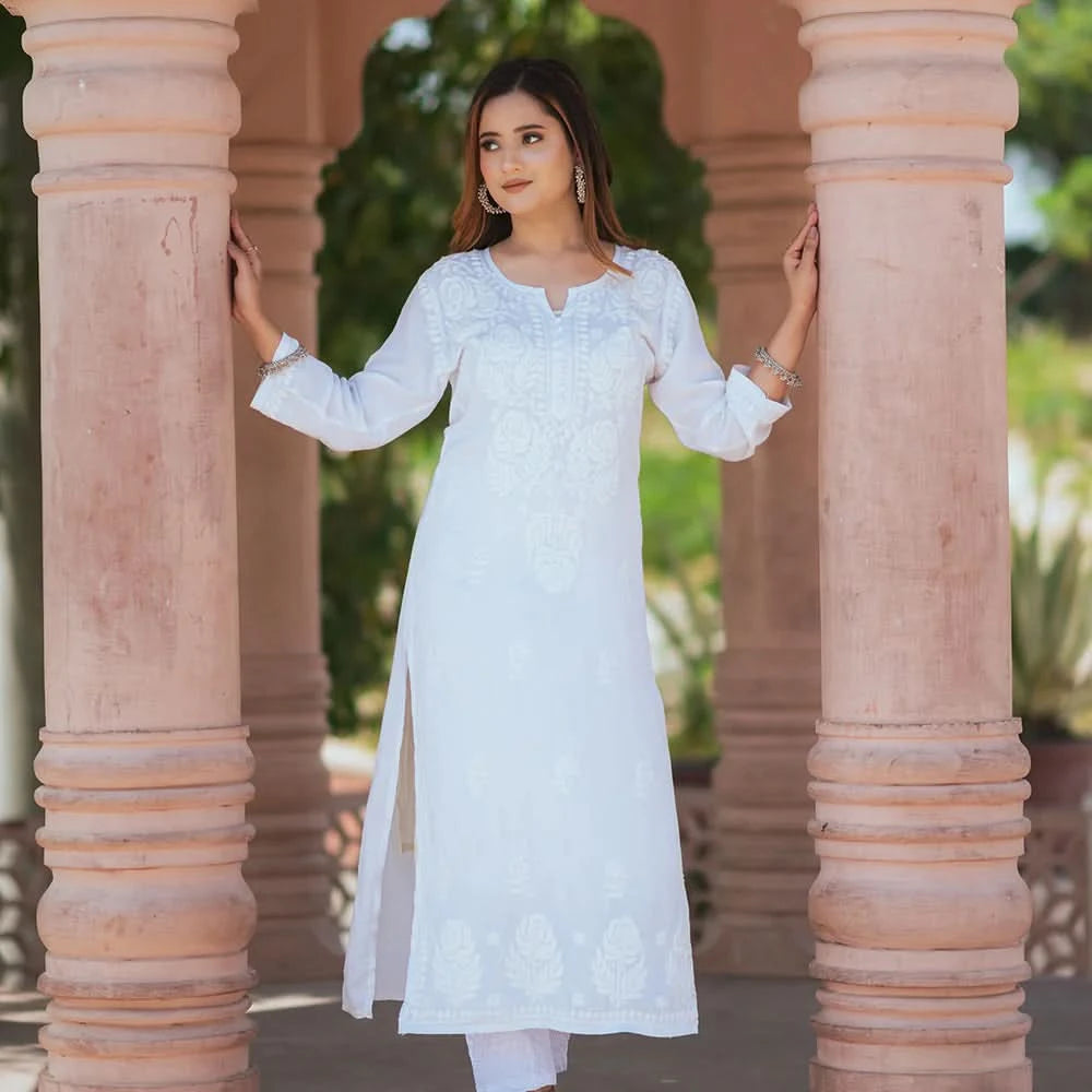 Woman in a white traditional outfit standing between two columns with greenery in the background