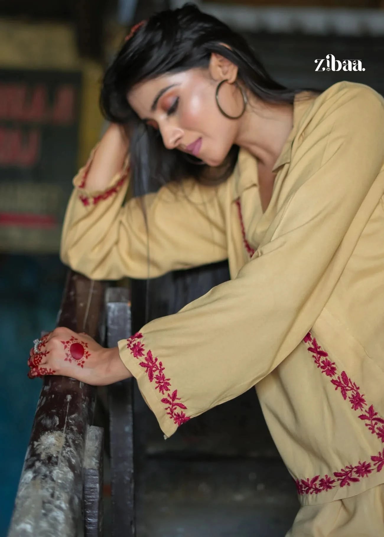 Model lifts arms to show full sleeves and border of the beige co-ord set with red embroidery. A perfect look for cultural functions and day events.