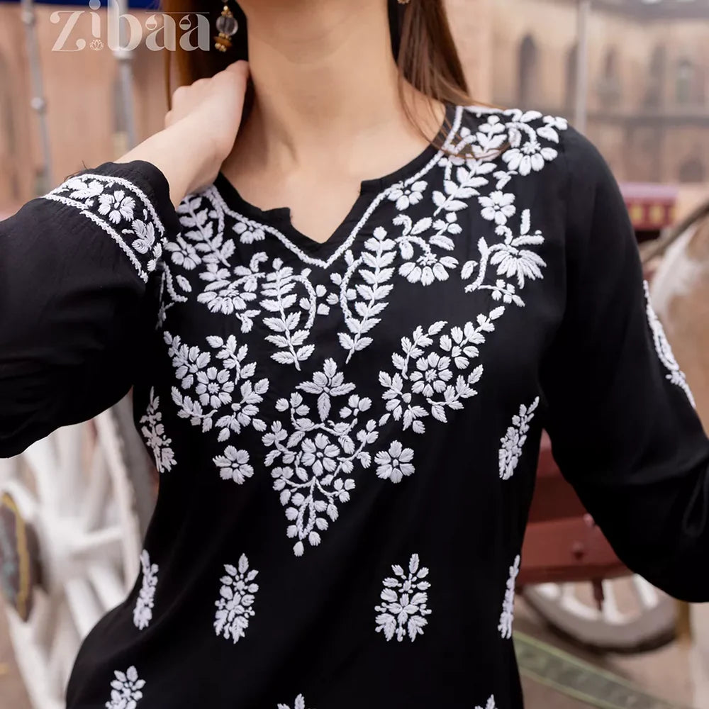 Black top with white floral embroidery worn by a person, blurred background