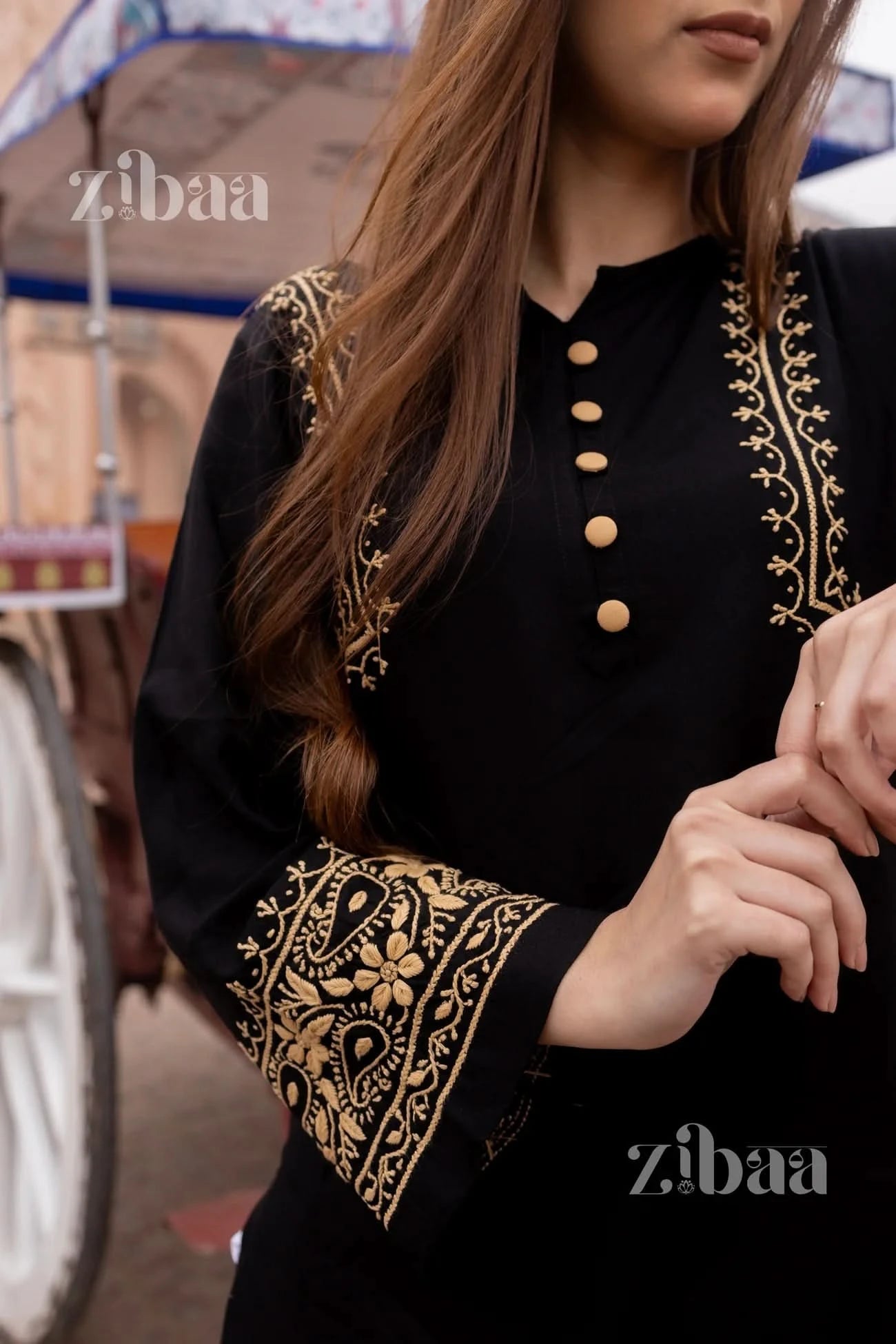 A close-up image of a woman wearing a black chikankari kurta with handcrafted golden brown embroidery. The kurta has a round neckline and the image showcases the fabric and the embroidery detail.