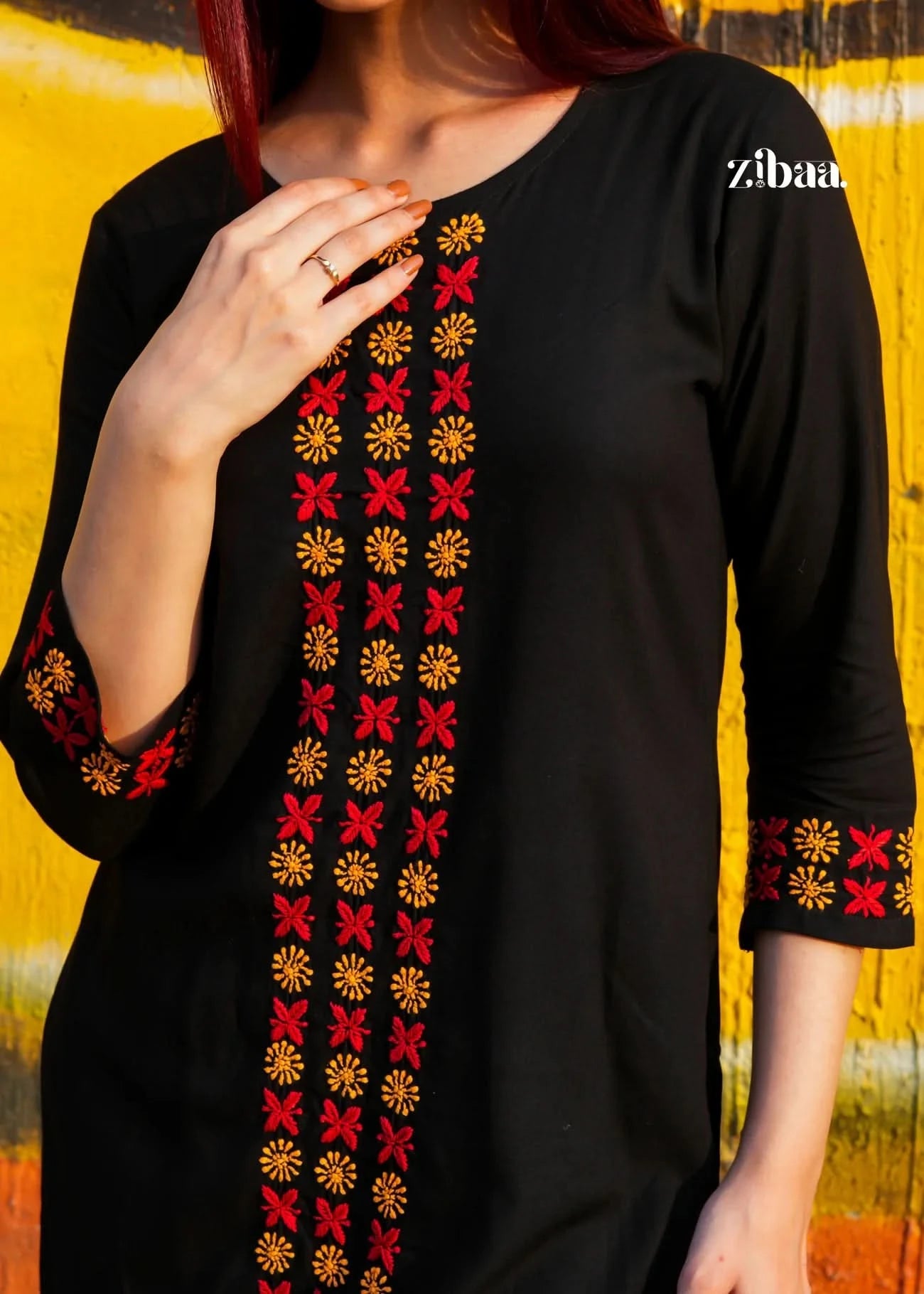 Close-up shot of a black chikankari kurti set with colorful embroidery against a yellow background.