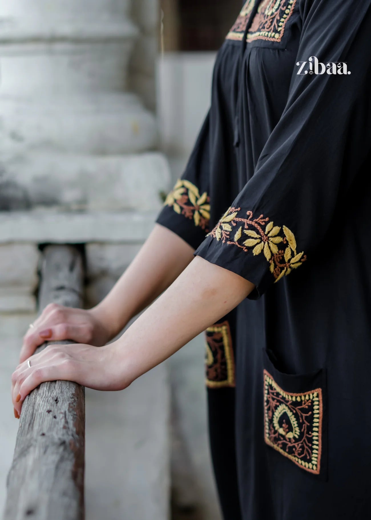 The model holds onto a railing, wearing a black chikankari kurti, while close-up shots highlight the intricate golden embroidery on the pockets, cuffs, and neckline.