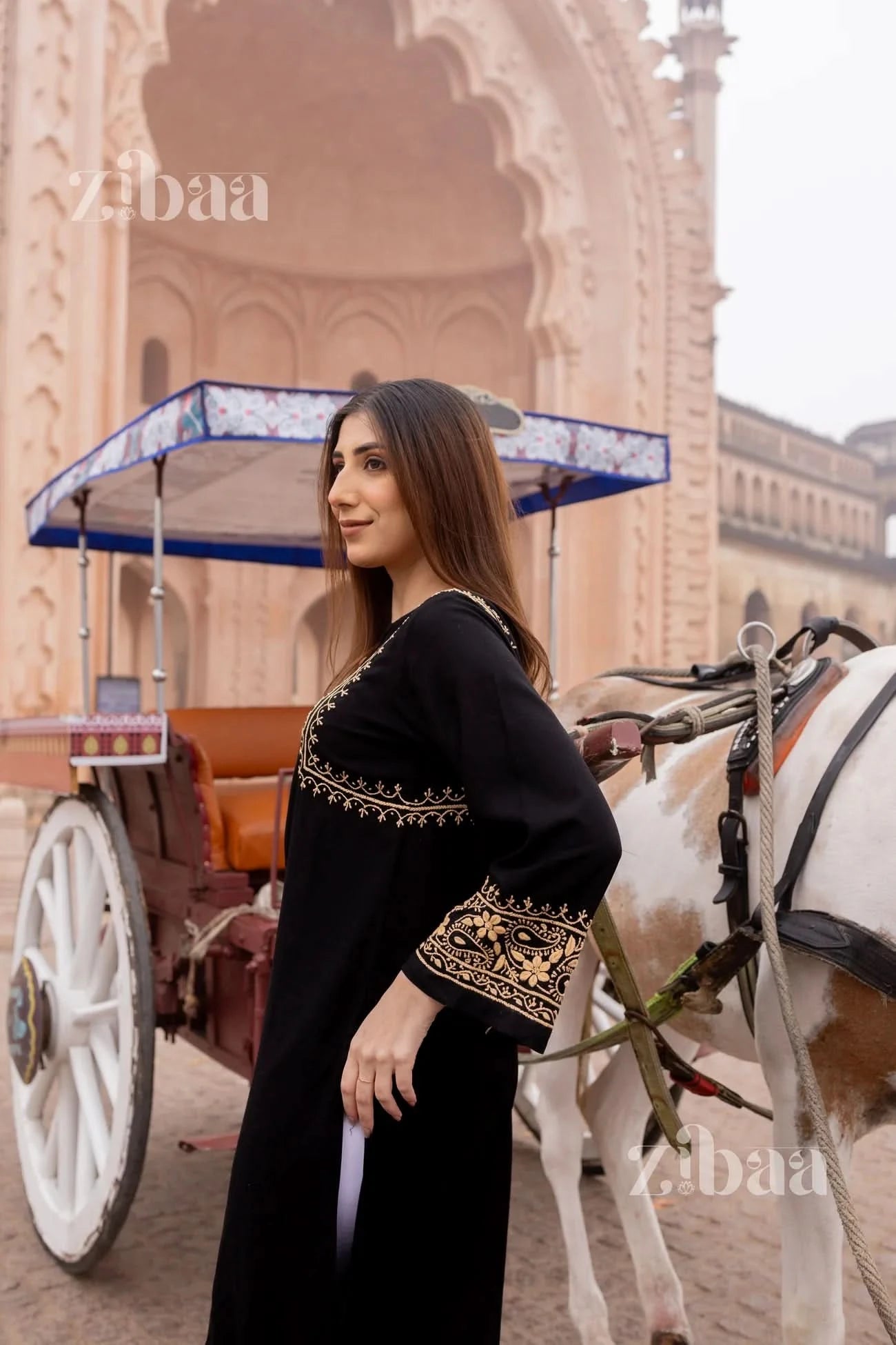 Side view of woman wearing a black chikankari kurti standing in front of an architectural backdrop