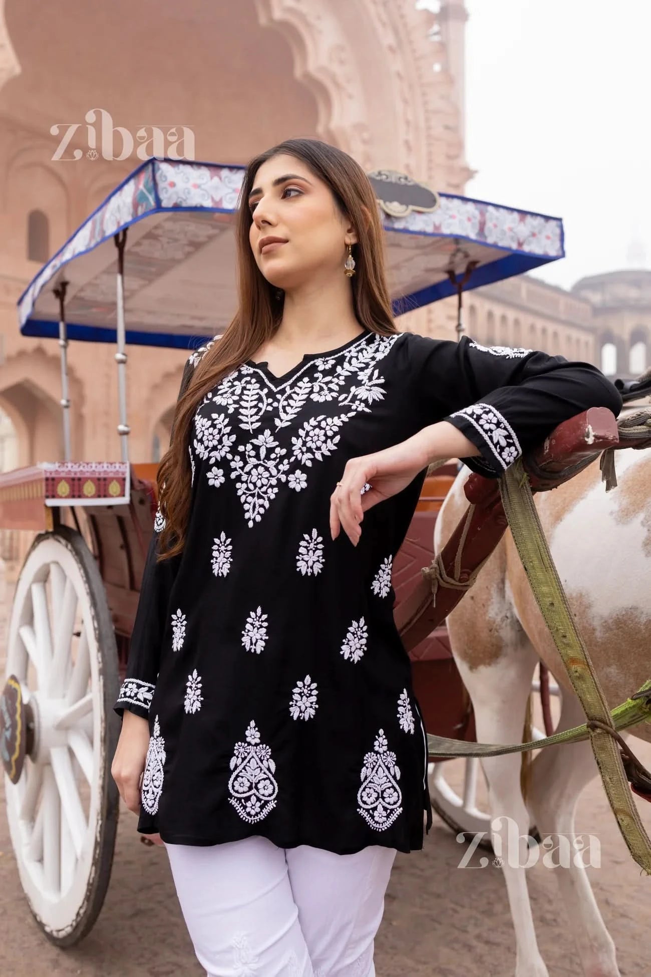 Woman wearing a black short chikankari kurti with a rickshaw in the backdrop.