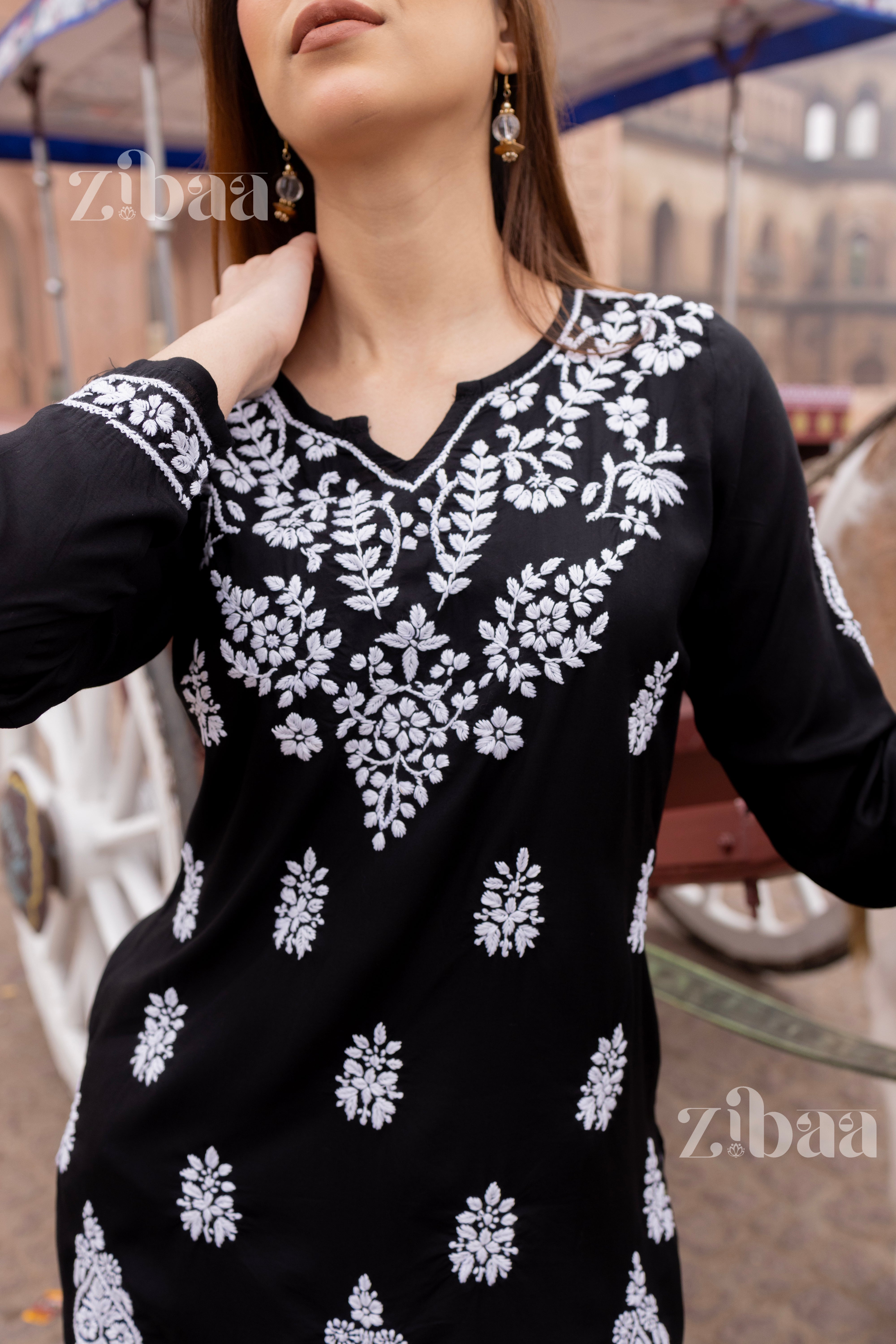 A woman wearing a black short chikankari kurti with floral embroidery.