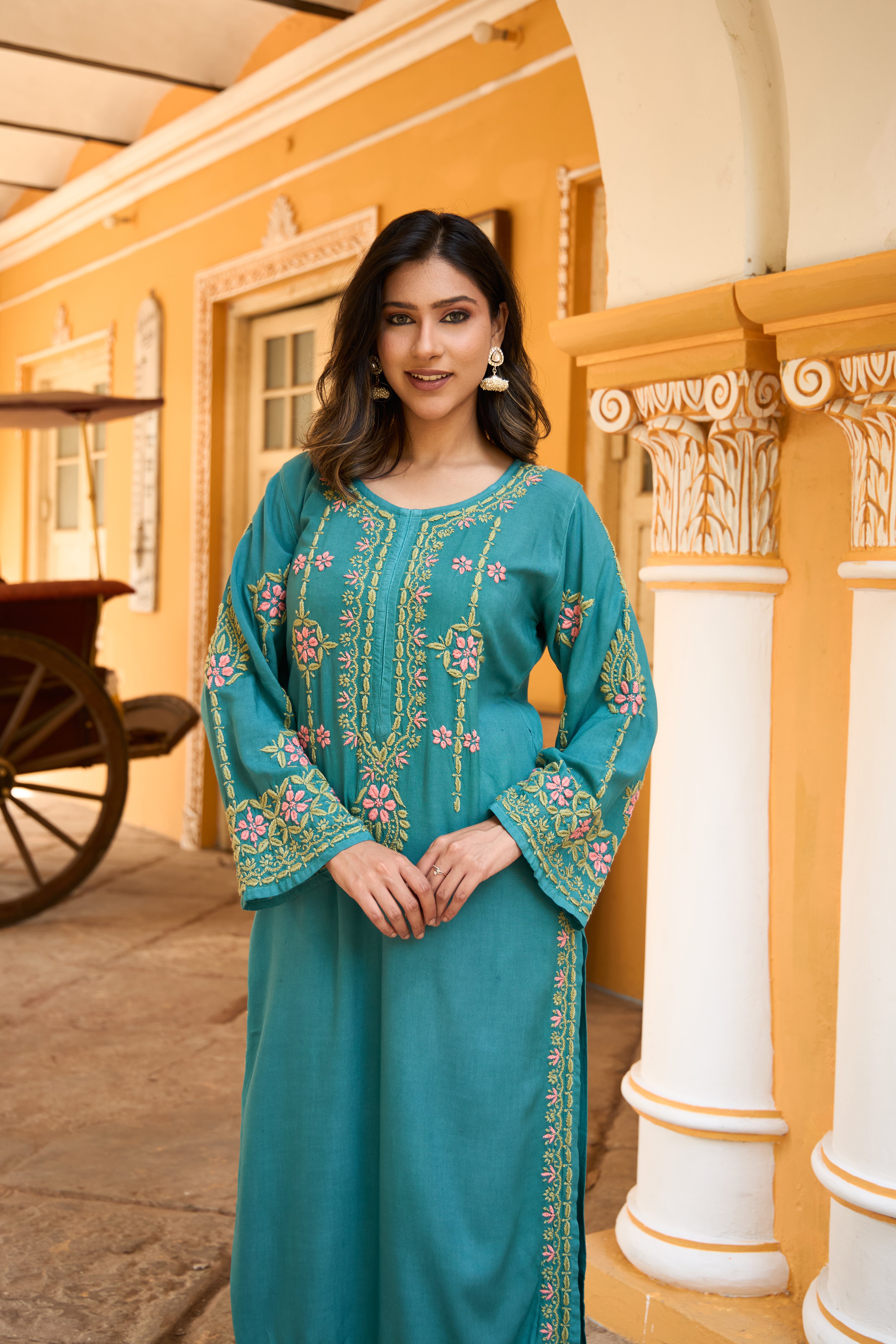 Woman in a teal Chikankari kurta set standing in front of a yellow building with white columns.