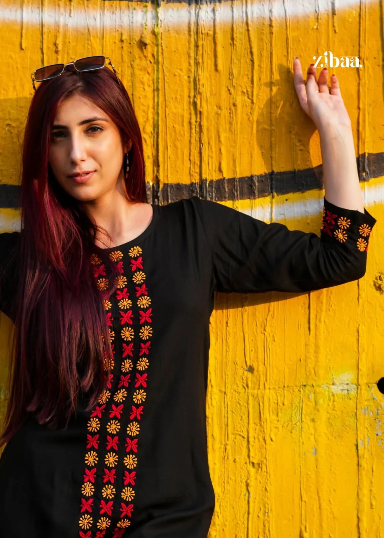Woman wearing a black chikankari kurta set with colorful embroidery against a yellow wall.
