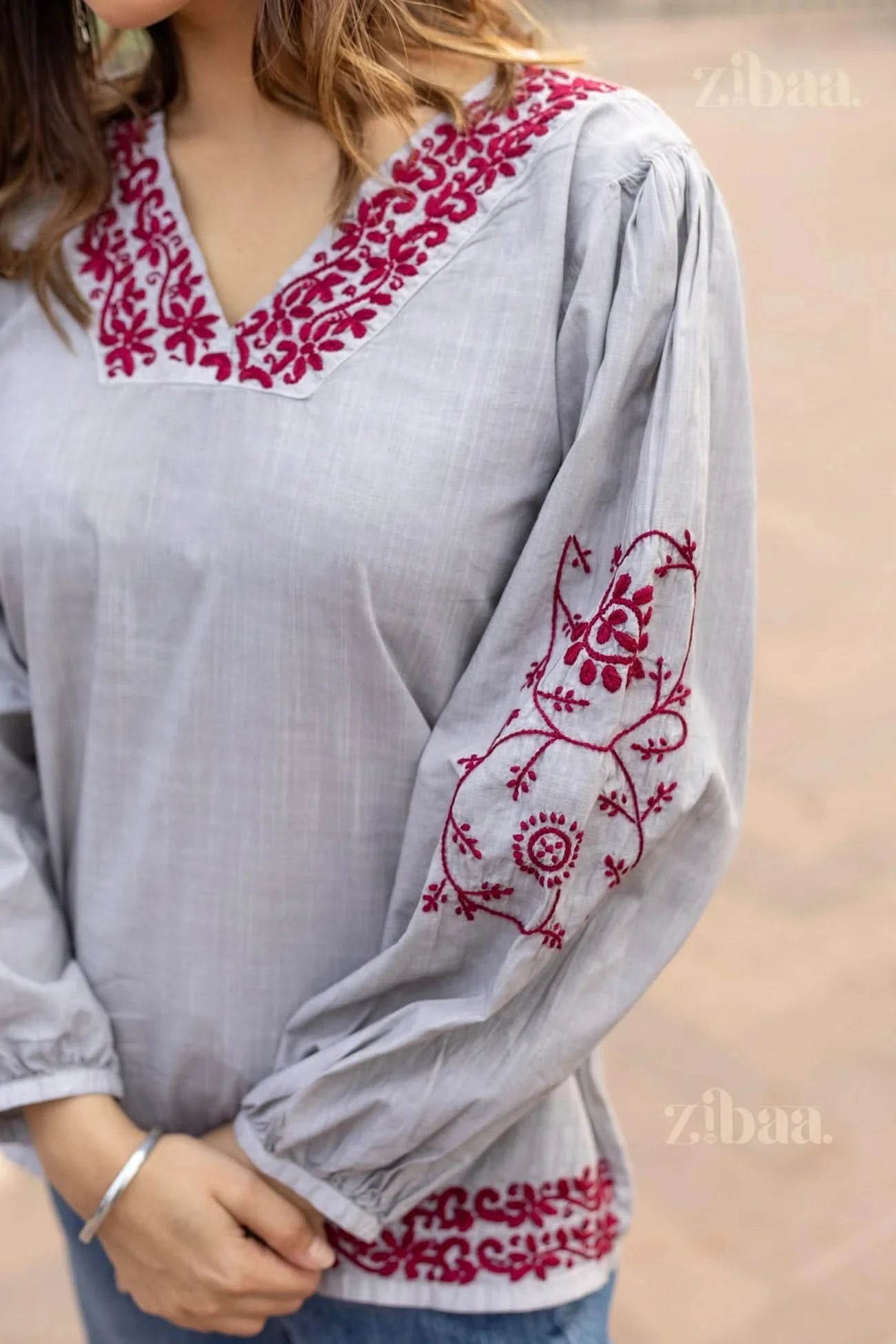 Front view of a woman posing in a grey Chikankari top with intricate red floral embroidery on the neckline, sleeves, and hemline