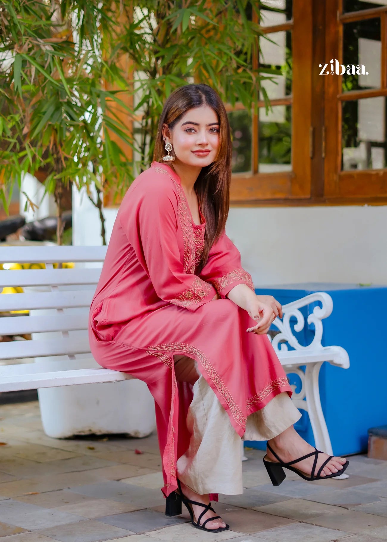 The model sits on a white bench wearing a coral chikankari kurti that highlights the fine chikankari stitching.