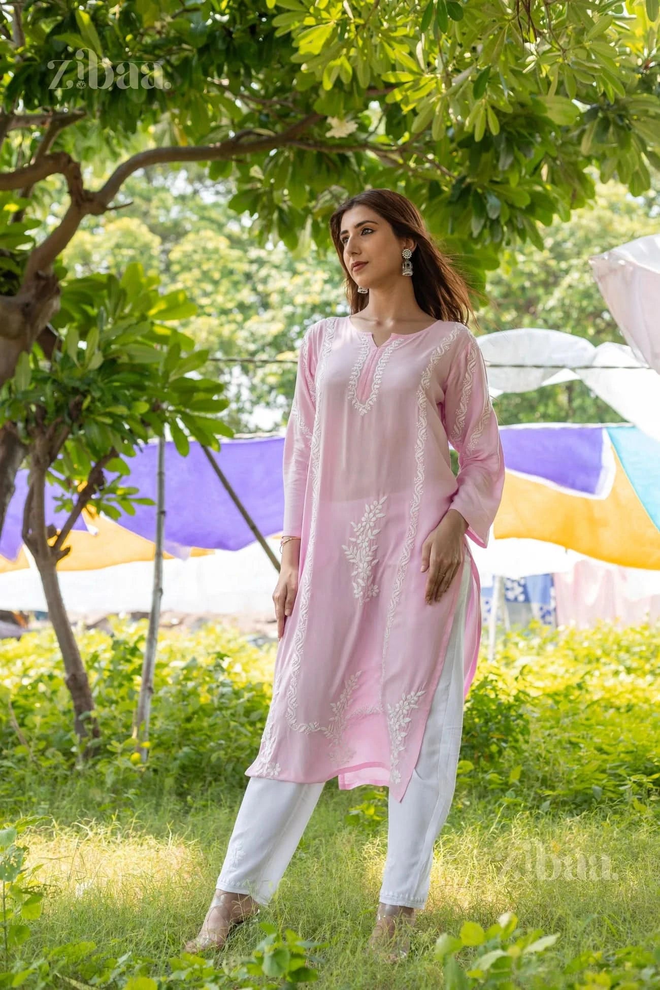 Model wearing a Pink Chikankari Kurti with delicate white embroidery, posing elegantly in a lush green outdoor setting under a tree.