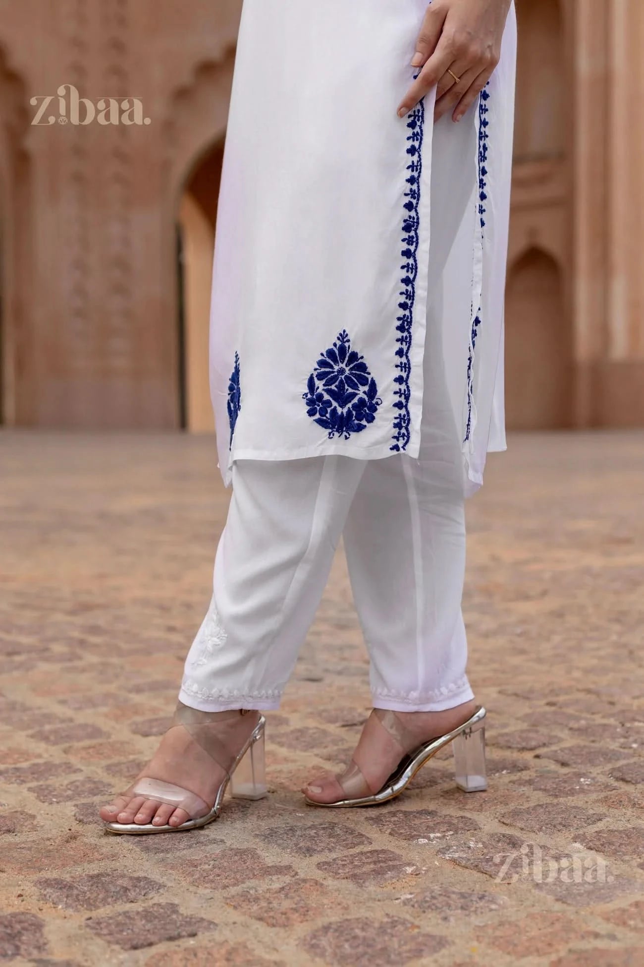 White outfit with blue embroidery on a textured ground, featuring the brand 'zibaa'.
