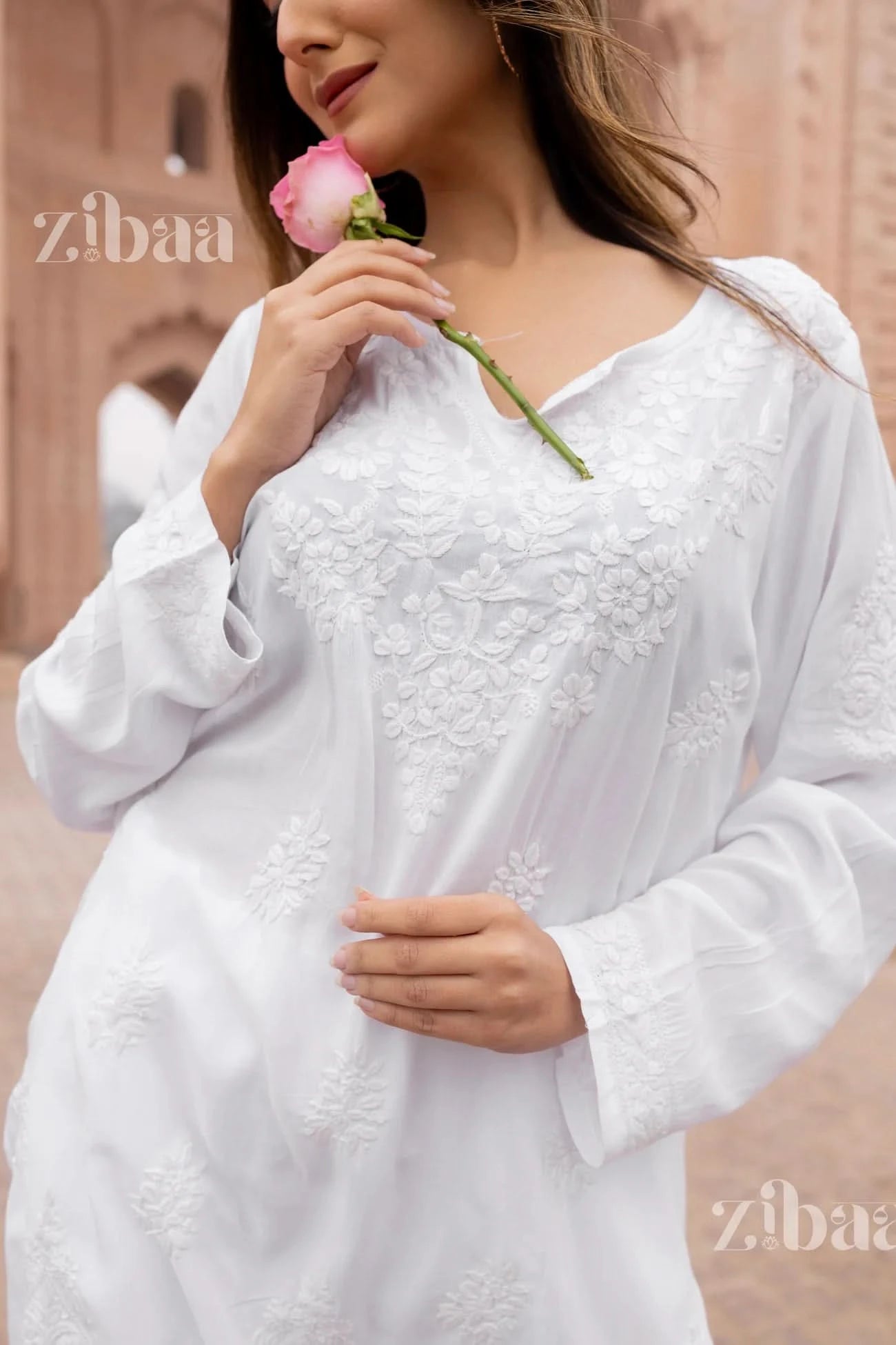 Woman in a white embroidered dress holding a pink rose, with 'zibaa' branding.