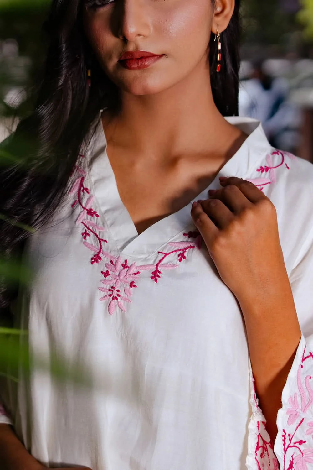 Detailed close-up of pink chikankari embroidery on the V-shaped neckline of a white kurti.