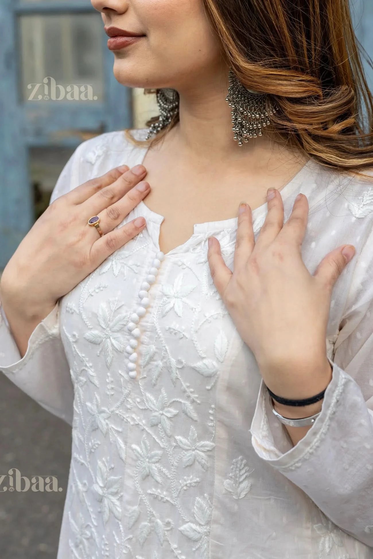 Close-up of a girl wearing a white Chikankari Anarkali with floral embroidery, touching the neckline with both hands, posing outdoors.