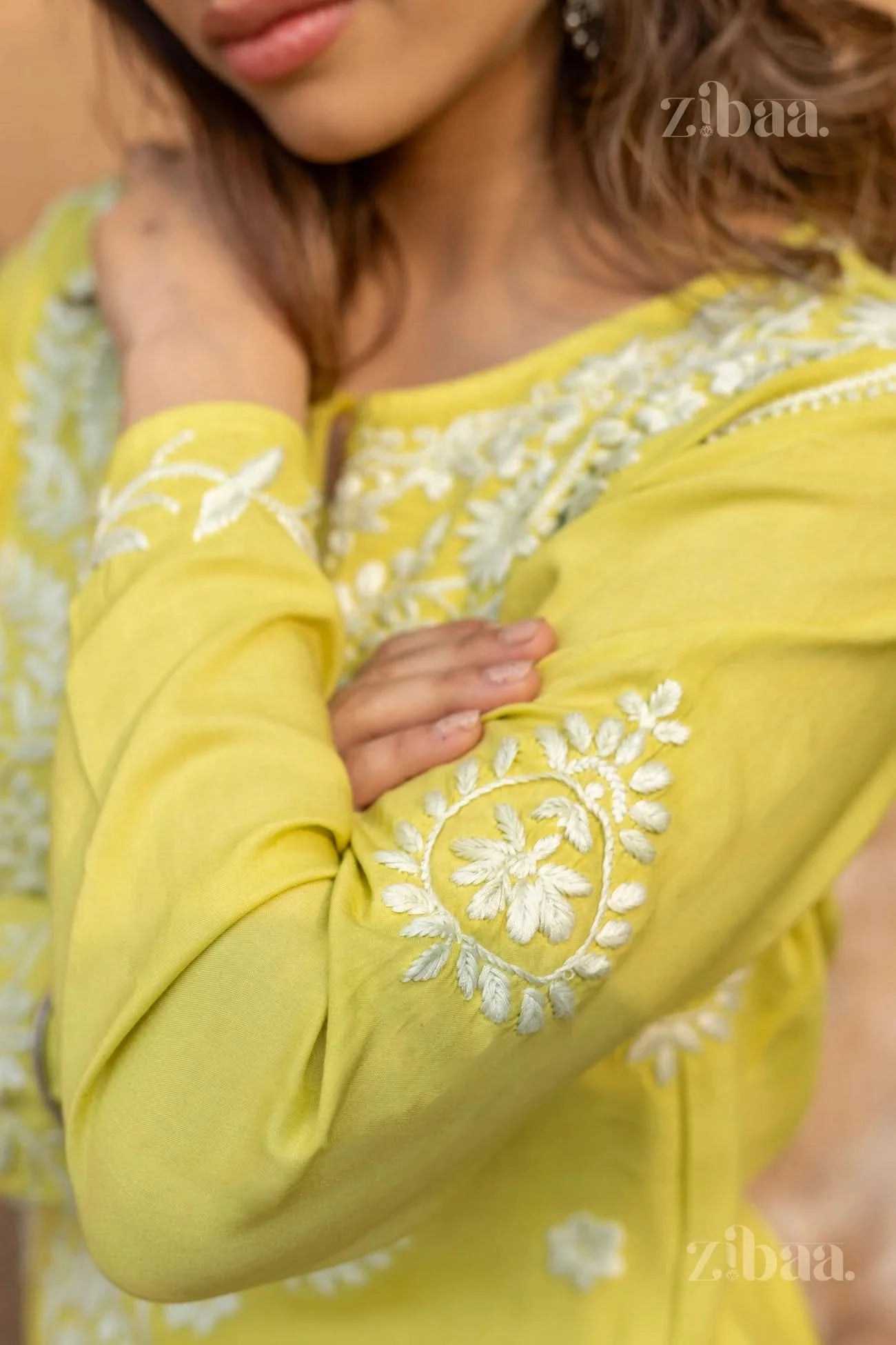 A close-up view of a woman resting her arm, showing the intricate white embroidery on the sleeve of a lime green Chikankari long kurti.
